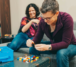 Breanne builds Lego while Jill looks on from the background, smiling.