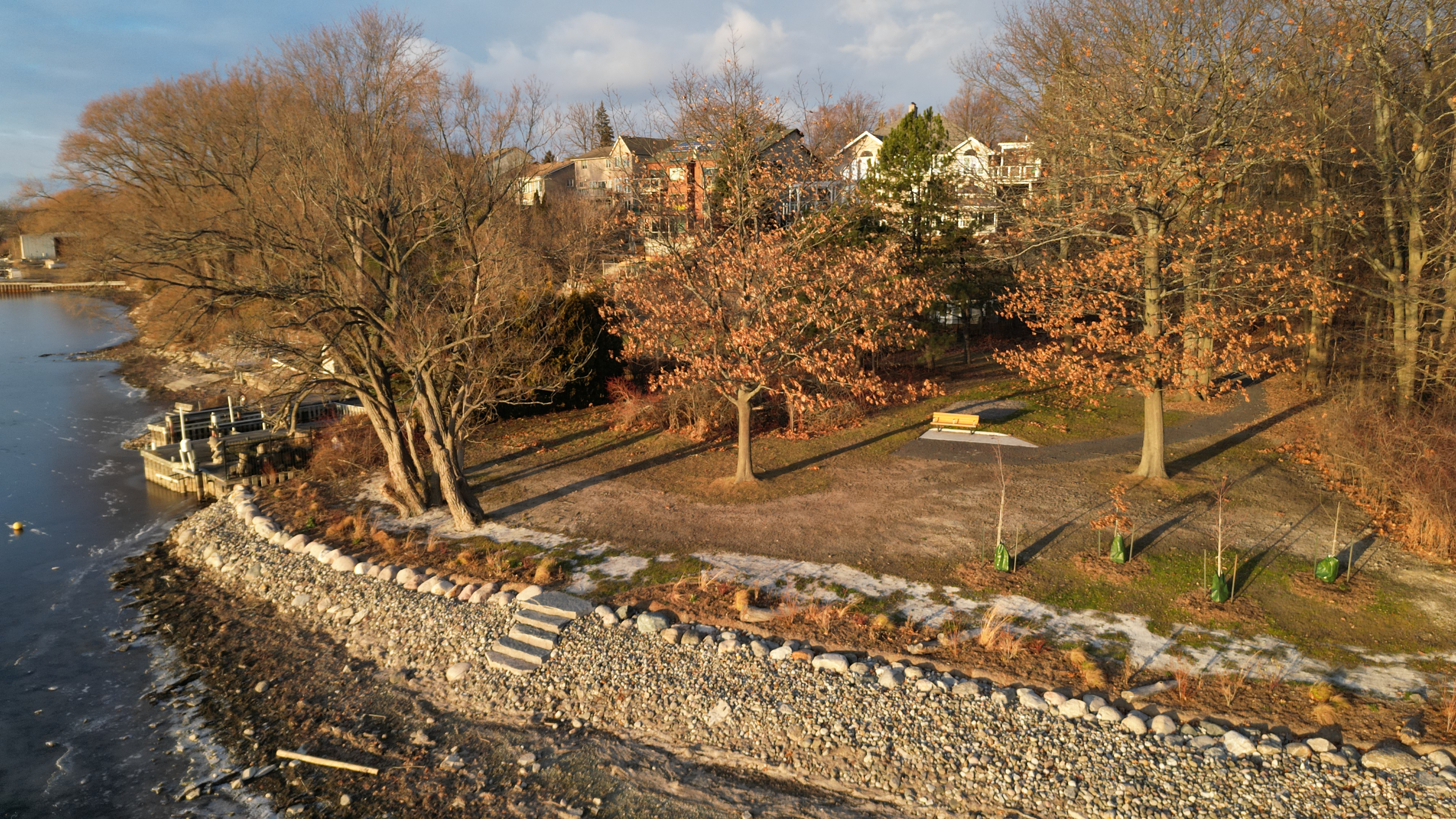 overhead view of a waterfront park with trees and a stone shoreline going down to the water.