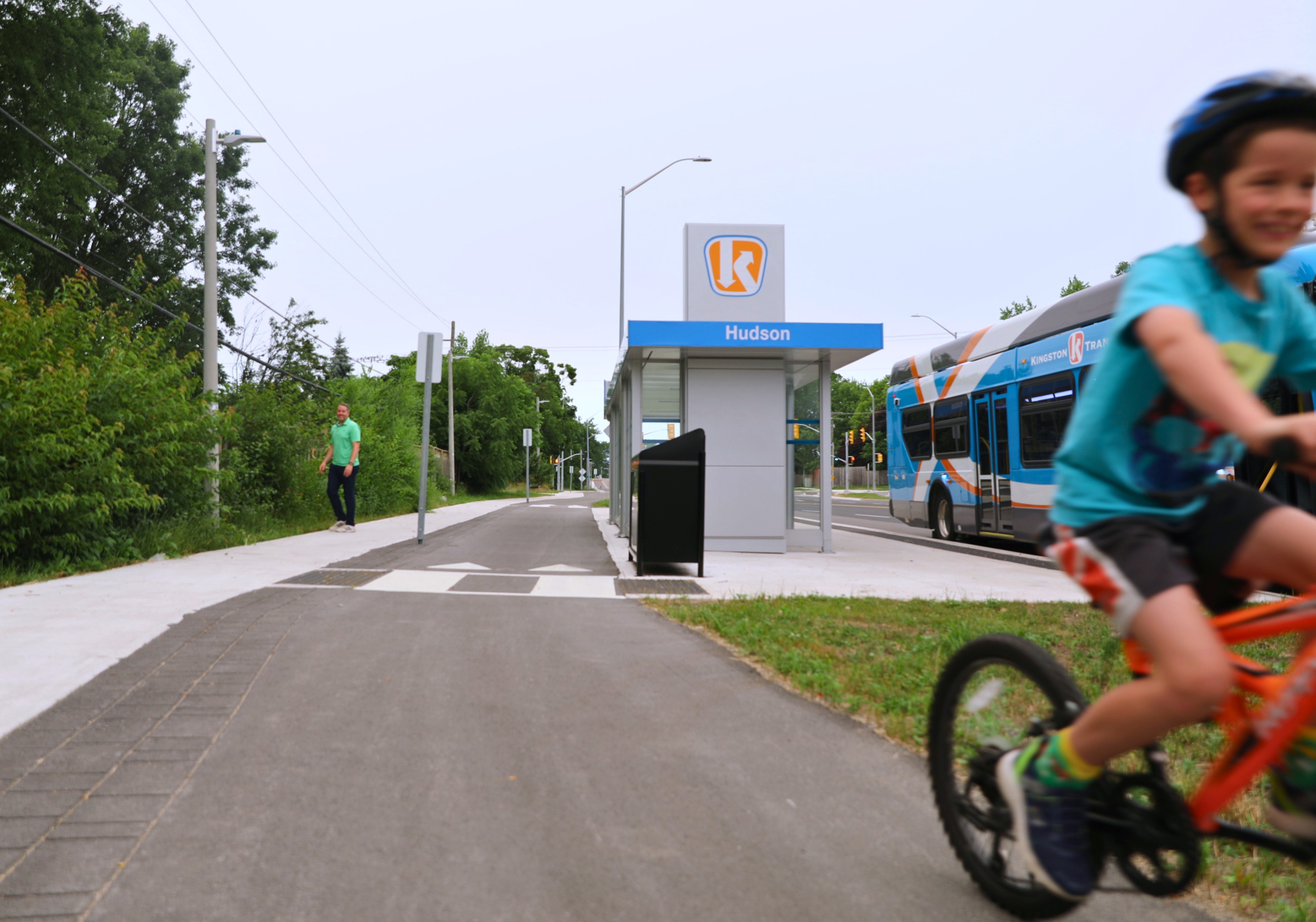 New pedestrian path and a bus stop on Bayridge Drive. A child in a blue shirt rides a red bike with a smile on their face.