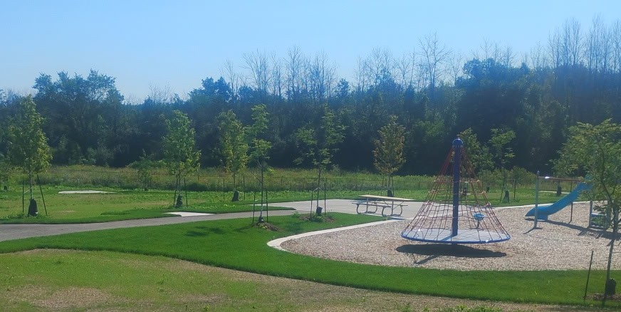 Creekside Valley park, featuring a climbing structure, slide, a picnic table, pathway and vegetation.