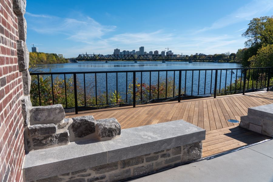 Gros plan sur le mur en pierre de la station de pompage historique d'Hintonburg, avec la rivière des Outaouais et le centre-ville d'Ottawa en arrière-plan, lors de l'événement d'inauguration le 2 octobre 2025.