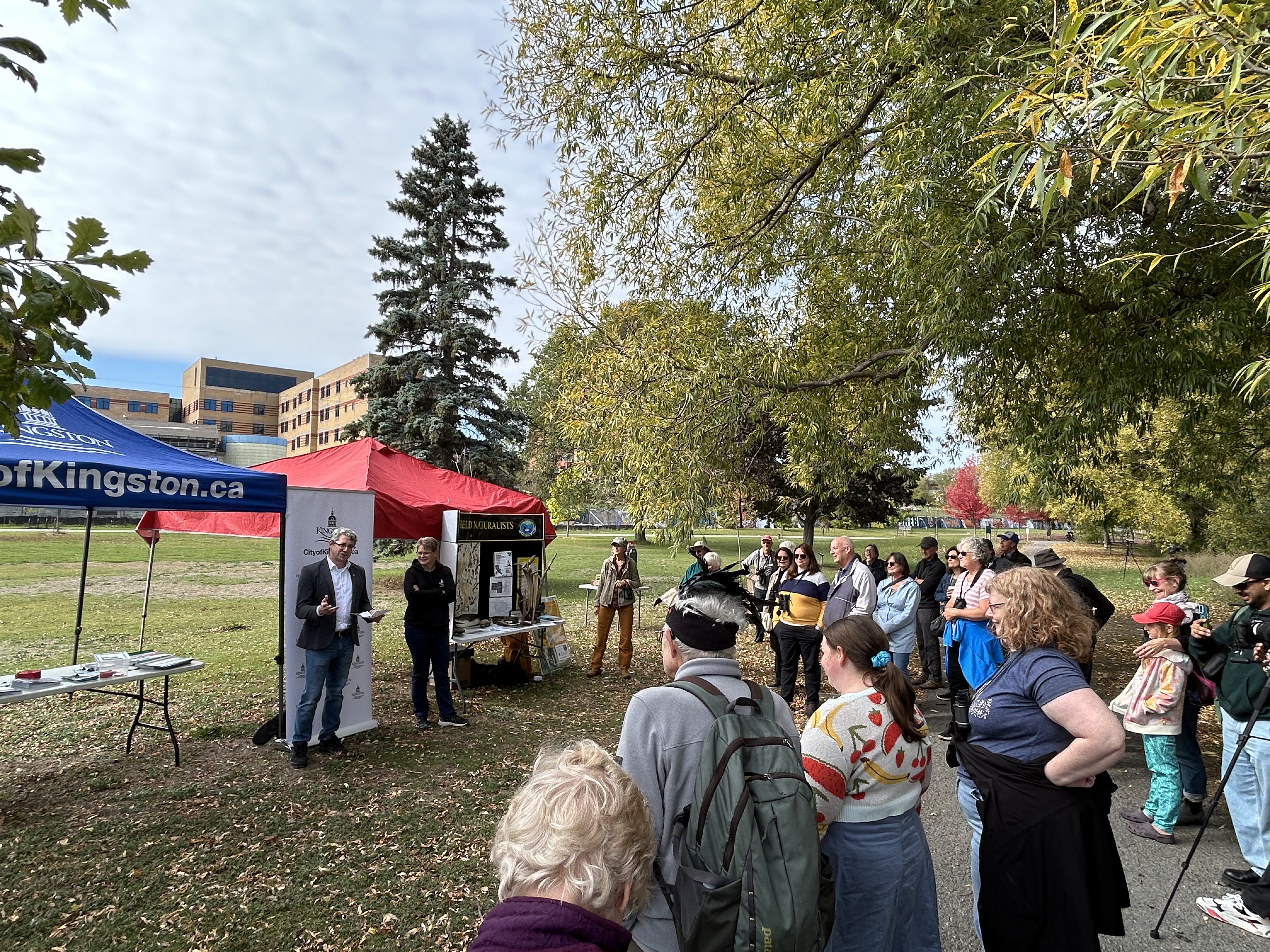 Kingston Councillor Gregory Ridge and Director of Public Works and Solid Waste Karen Santucci stand speaking to a crowd in front of tents from the City of Kingston and Kingston Field Naturalists.