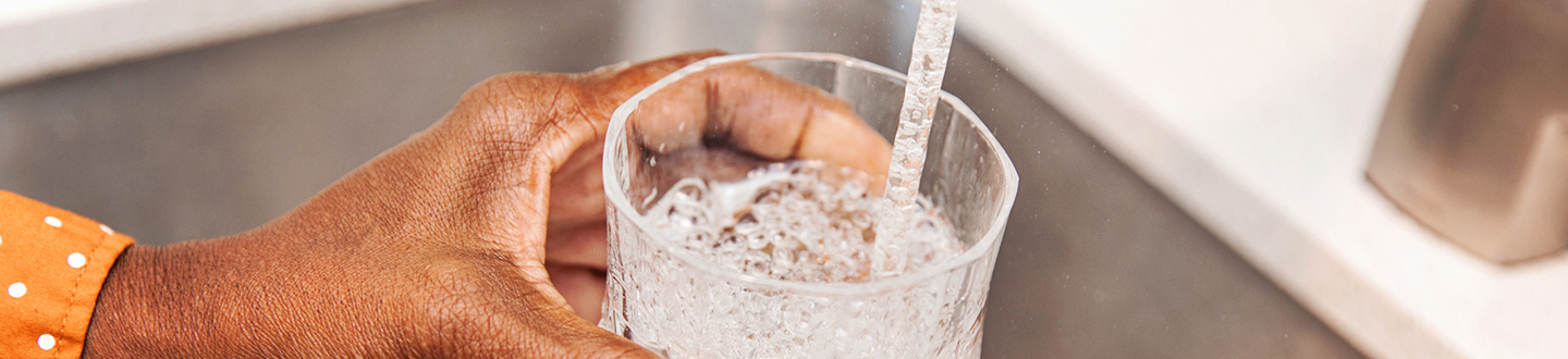 Person filling up a glass of water from a kitchen tap
