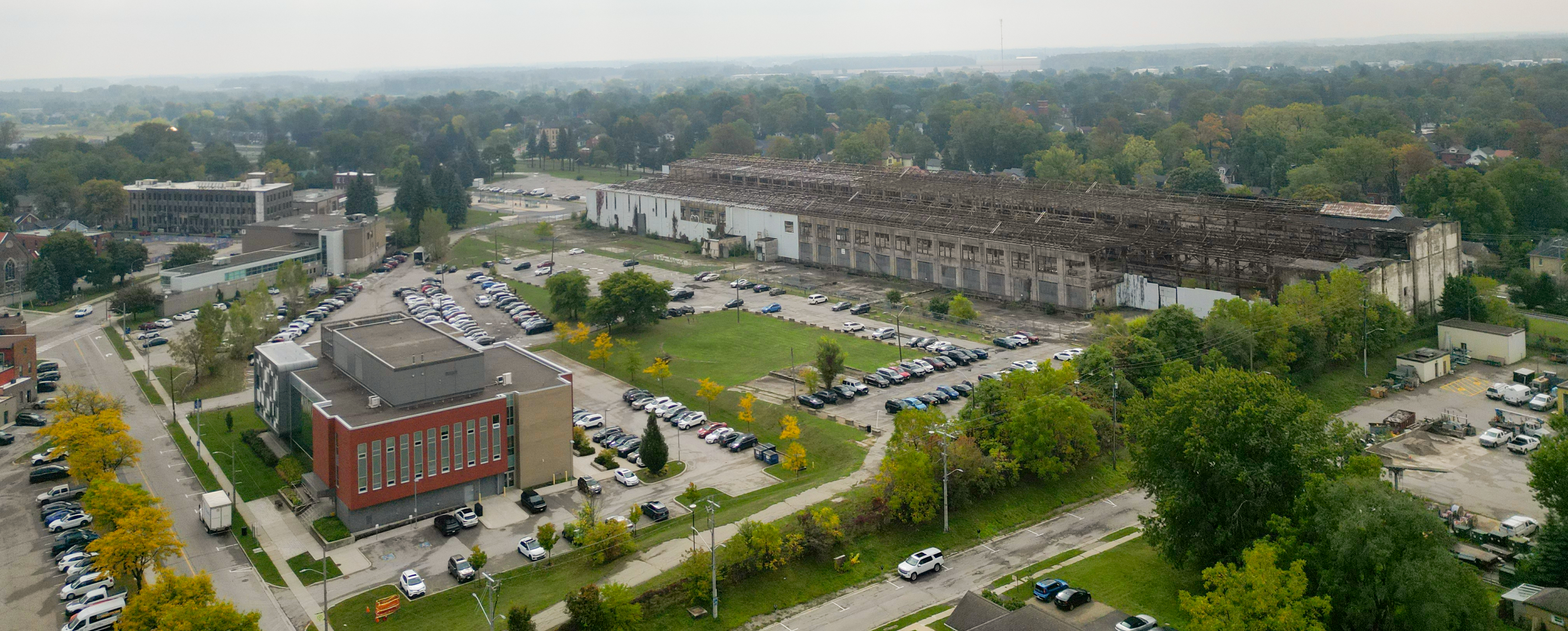 Colour, aerial photo of the Grand Trunk site in Stratford, Ontario (2025). Birds-eye view from a drone. Shows the University of Waterloo (Stratford Campus) in the foreground at bottom left and the structure in the background. The photo was taken on a gray, cloudy day. [Cropped]. Image ©Superkül, 2025.