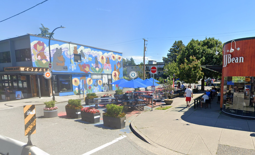 A side street where half the street is being used for for a patio space delineated by planter boxes.