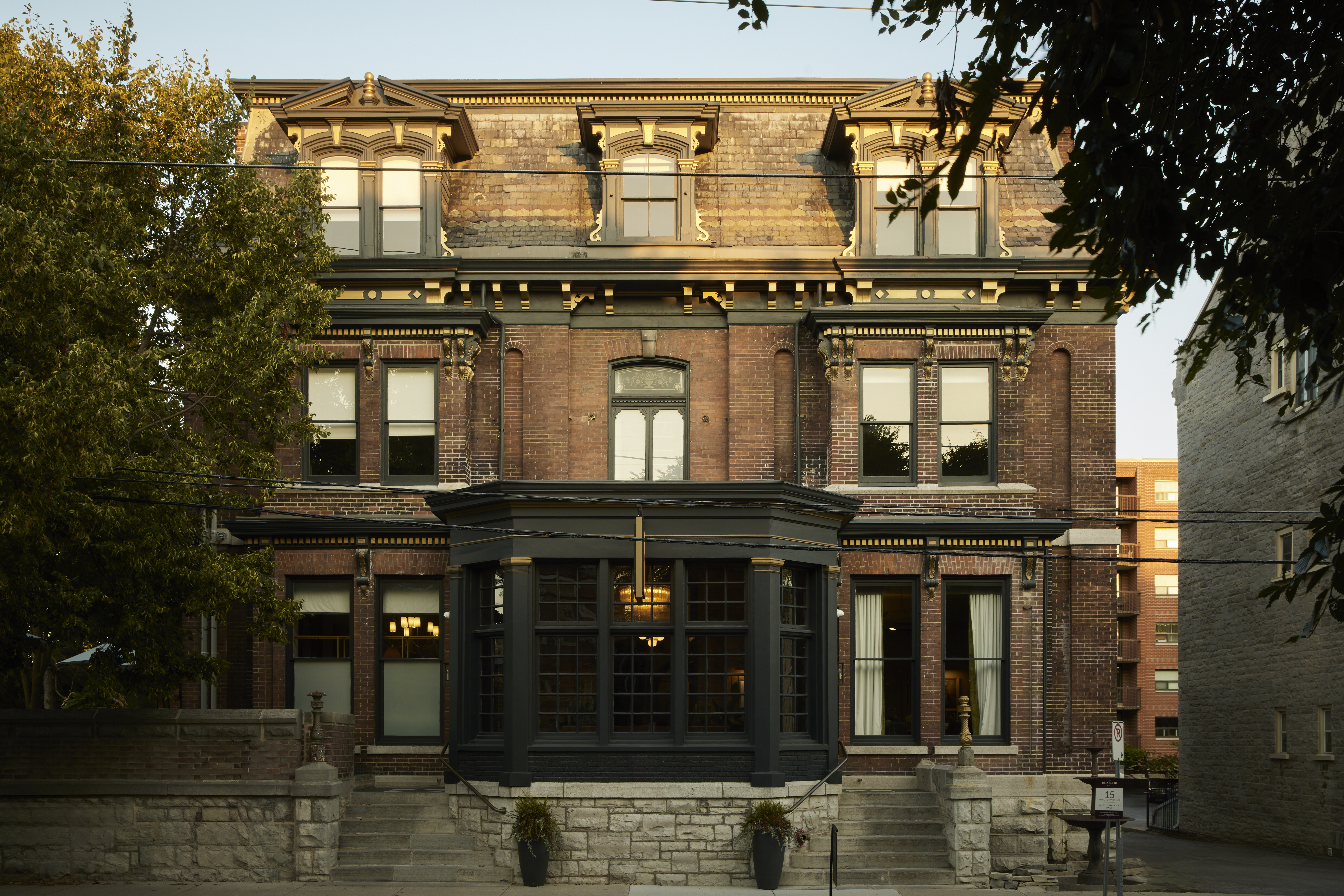 A stately dark red brick building with detailed woodwork and brickwork around the roof and windows. 