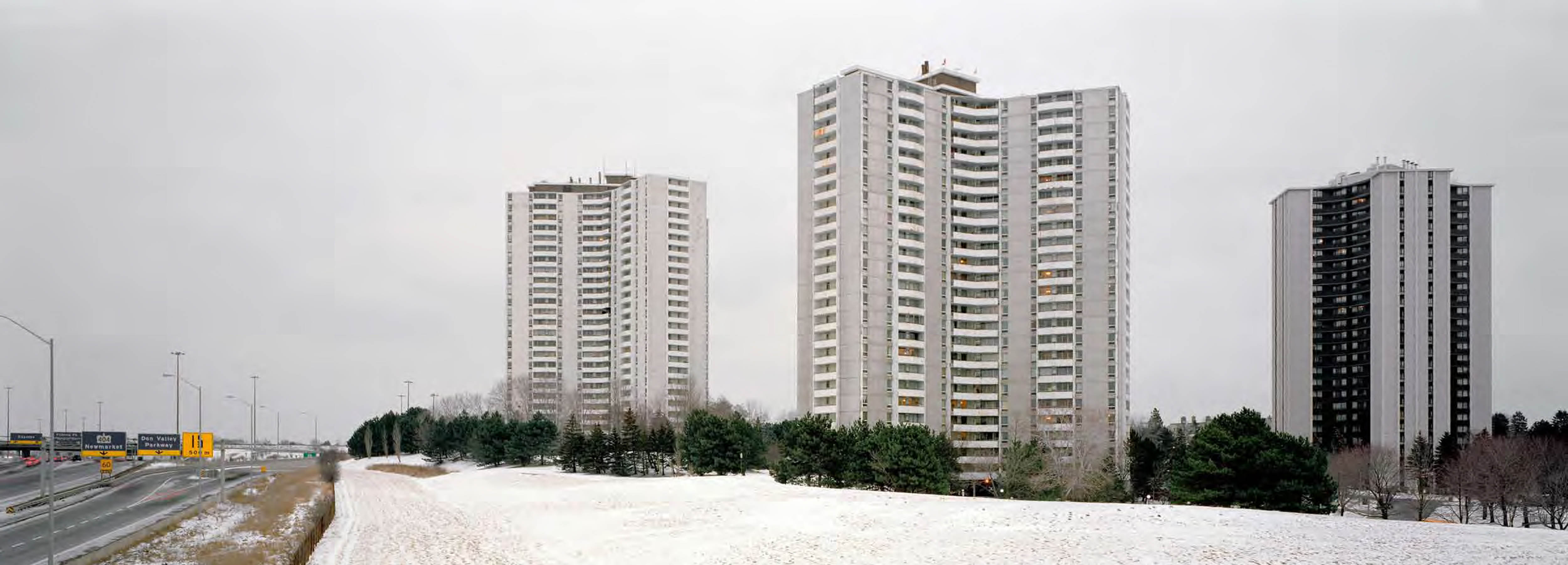 Tall apartment towers surrounded by trees and snow-covered lawns next to a highway