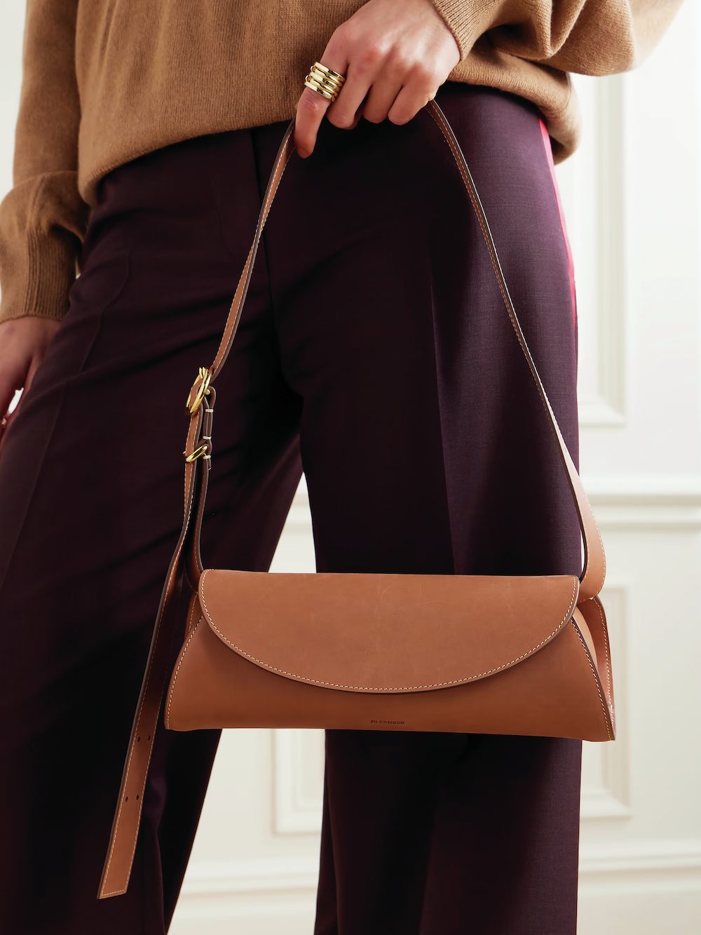 Brown leather shoulder bag held by a model wearing a cozy sweater and tailored pants, showcasing contemporary fashion trends and refined accessories for winter wardrobes.