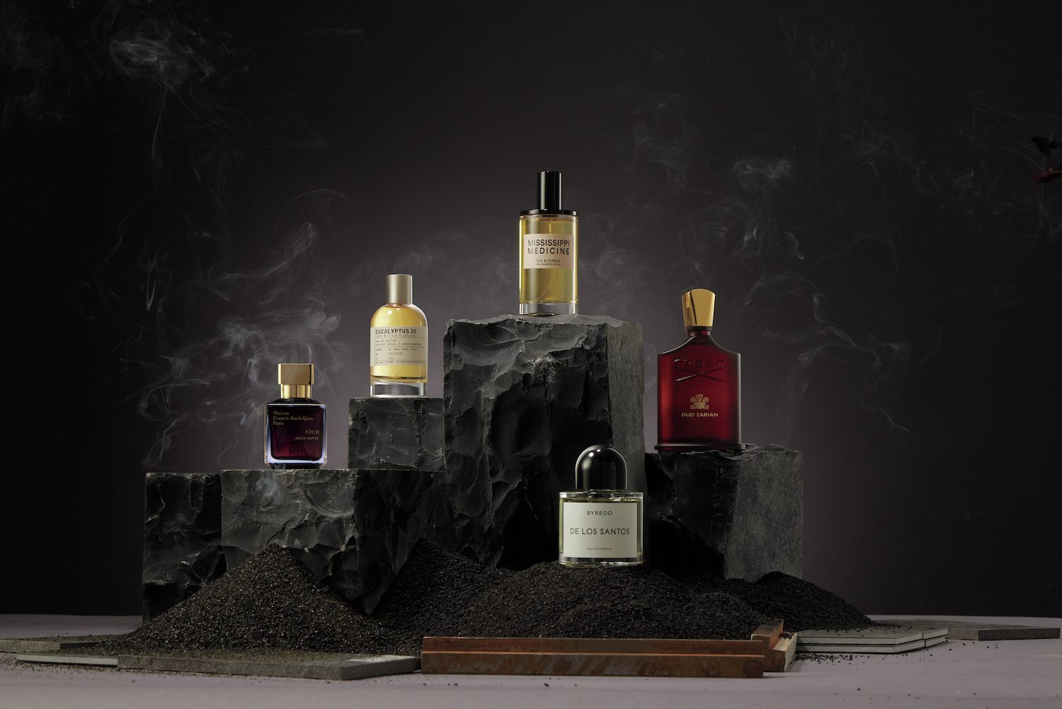 Modern fragrance bottles displayed on dark stone pedestals with aromatic smoke, highlighting luxurious scents and the intersection of beauty and spirituality in contemporary fragrance trends.