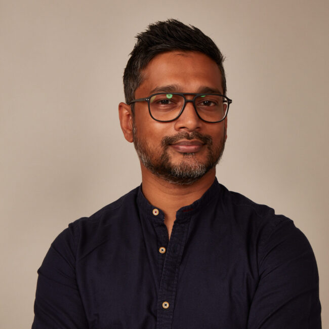 Muraly Srinarayanathas, publisher and founder of Three Magazine, posing confidently in a navy shirt against a neutral background, representing the magazine's focus on multicultural identity and global narratives.