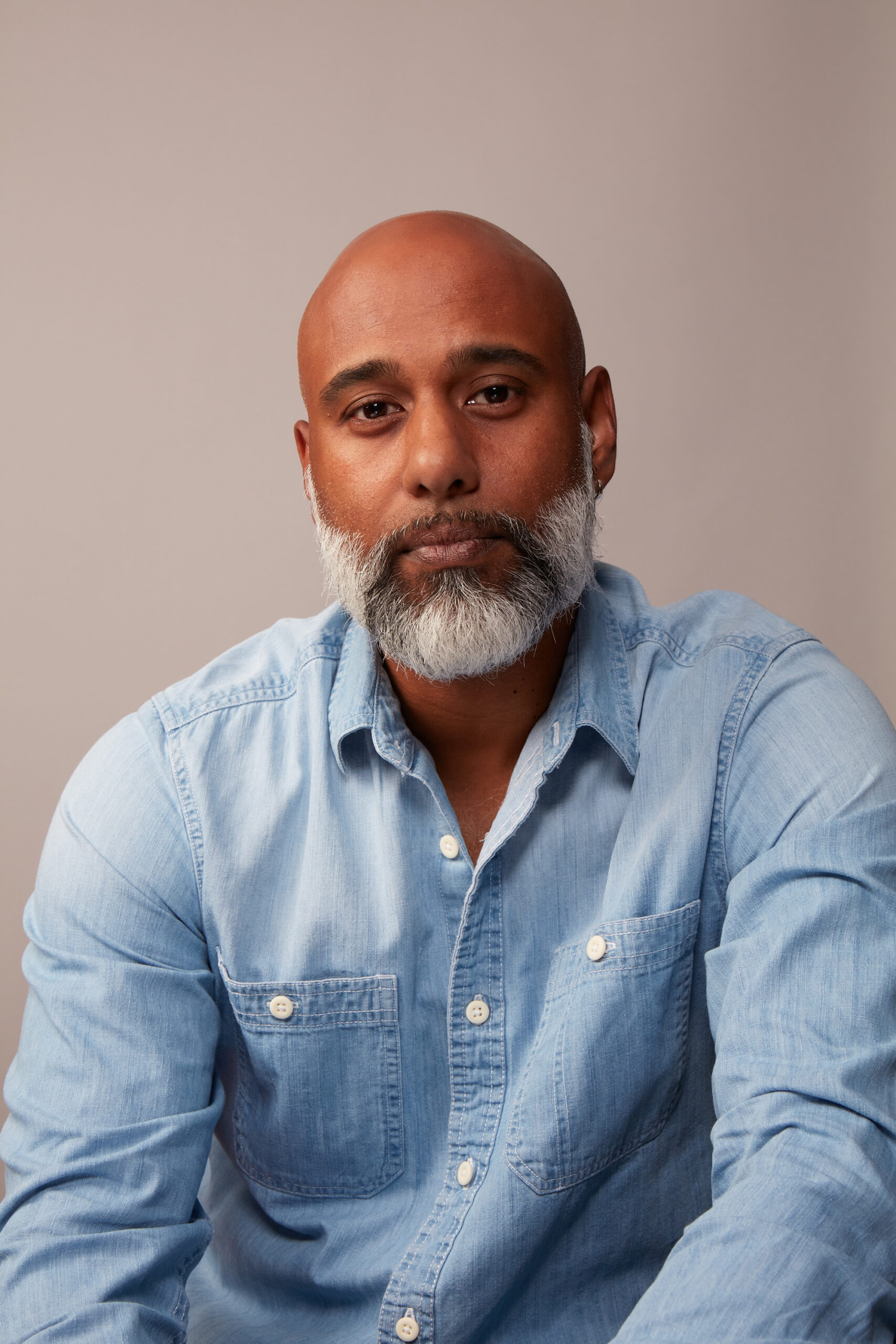 Muraly Srinarayanathas, an author featured in 3 Magazine, with a thoughtful expression, wearing a light blue denim shirt, against a neutral background, reflecting themes of identity and immigration.