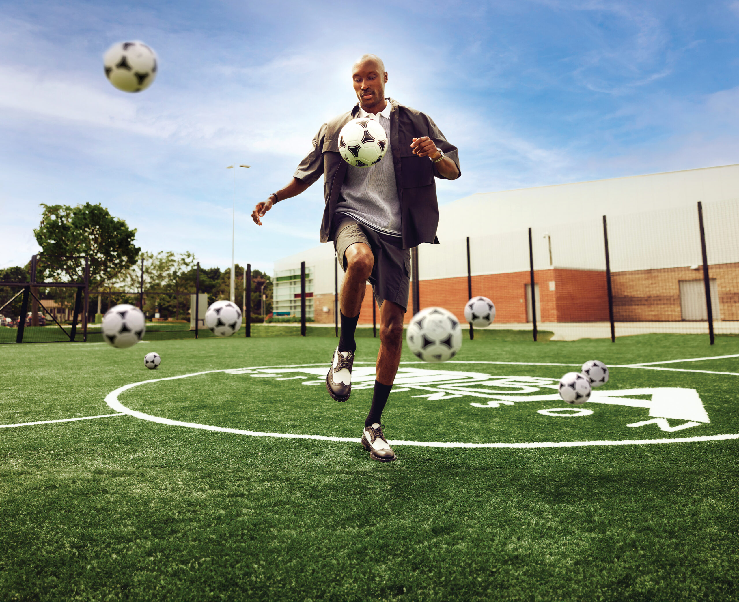 Atiba Hutchinson playfully juggling soccer balls on a green pitch, showcasing athleticism and style in a casual outfit.