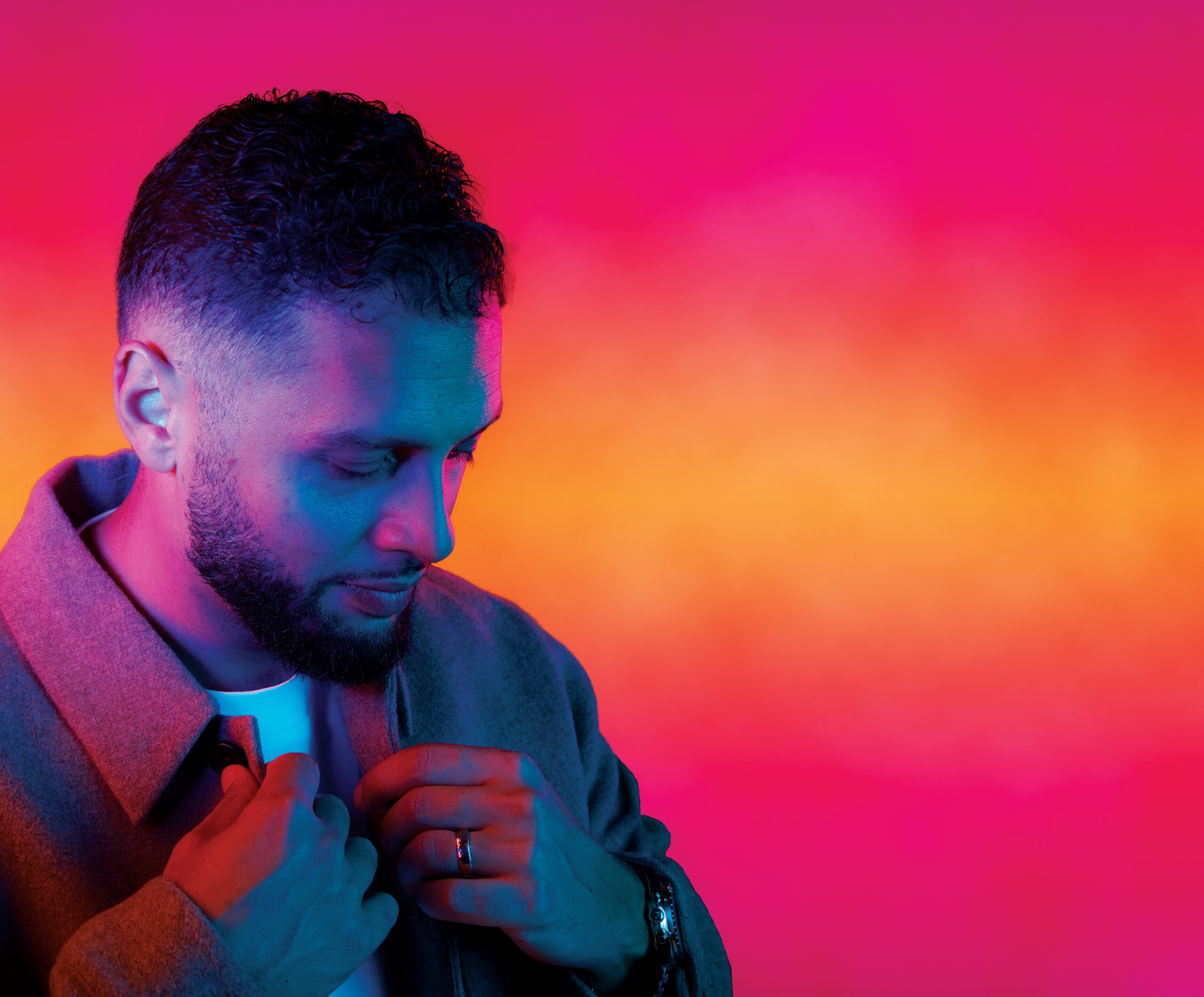 Abdullah Snobar in a stylish gray jacket, adjusting his collar against a vibrant pink and orange gradient background, reflecting his innovative leadership in the tech industry.