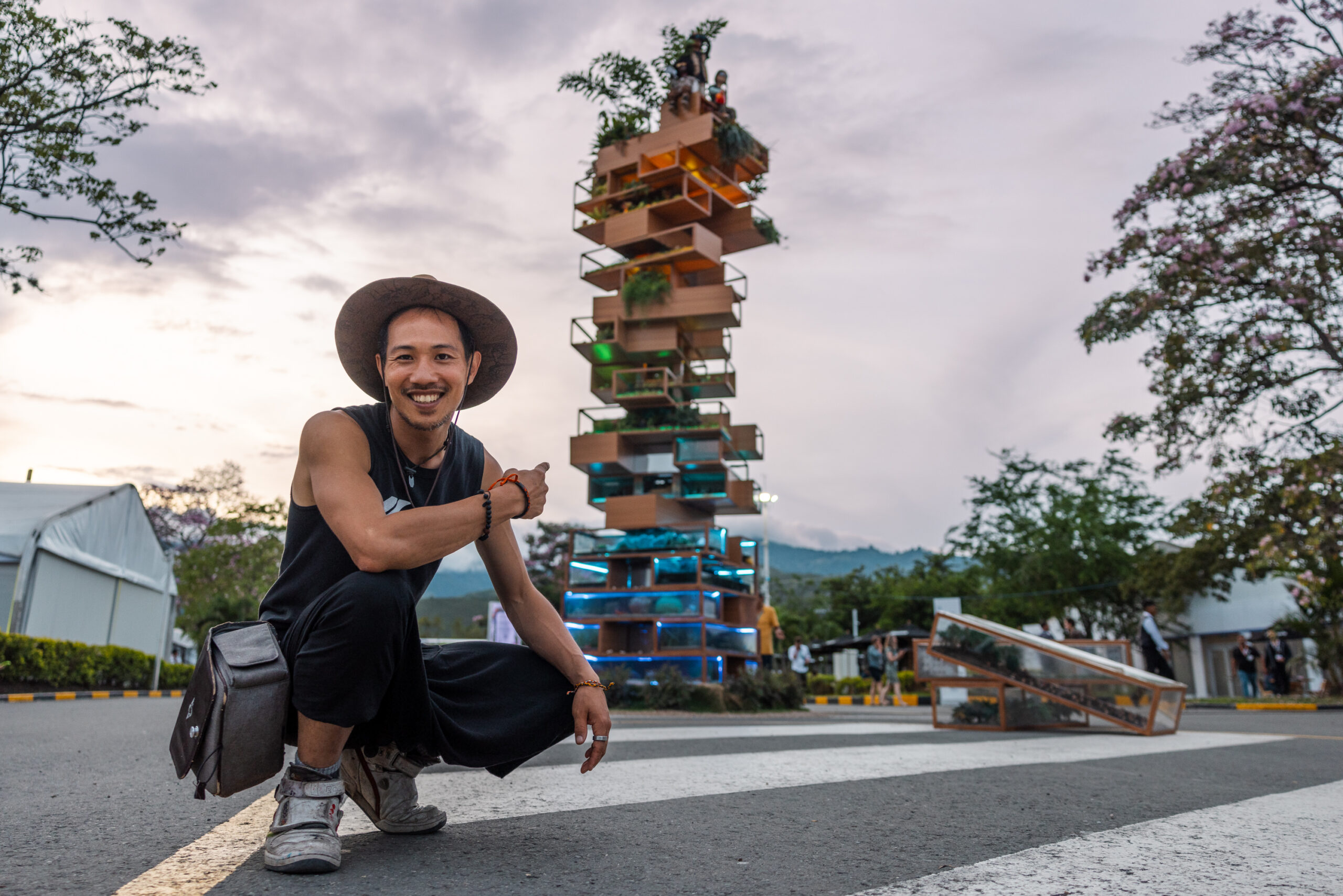 Artist Benjamin Von Wong posing in front of a large-scale, eco-friendly installation featuring stacked planters and greenery, highlighting environmental activism.