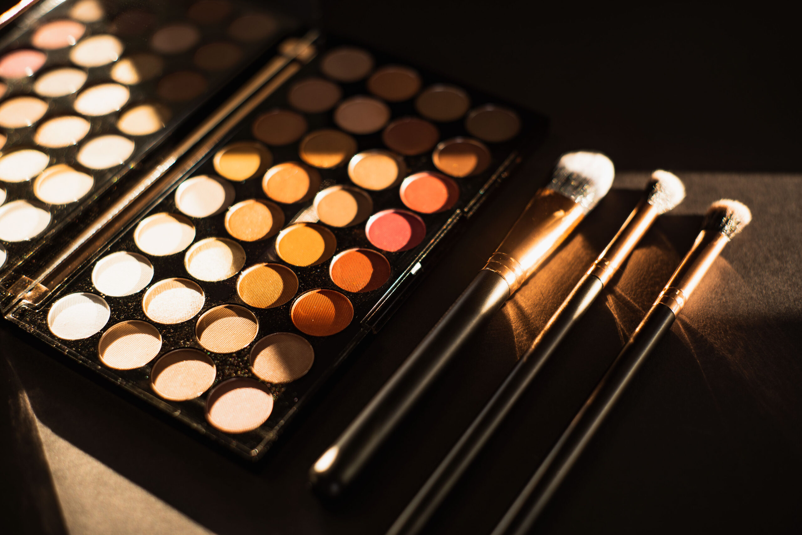 Makeup palette with warm-toned eyeshadows and three makeup brushes, emphasizing beauty and style.