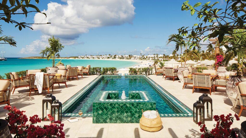 Luxurious outdoor dining area at Maundays Club, featuring a serene pool, tropical plants, and stunning beachfront views in Anguilla, evoking a cultural escape.