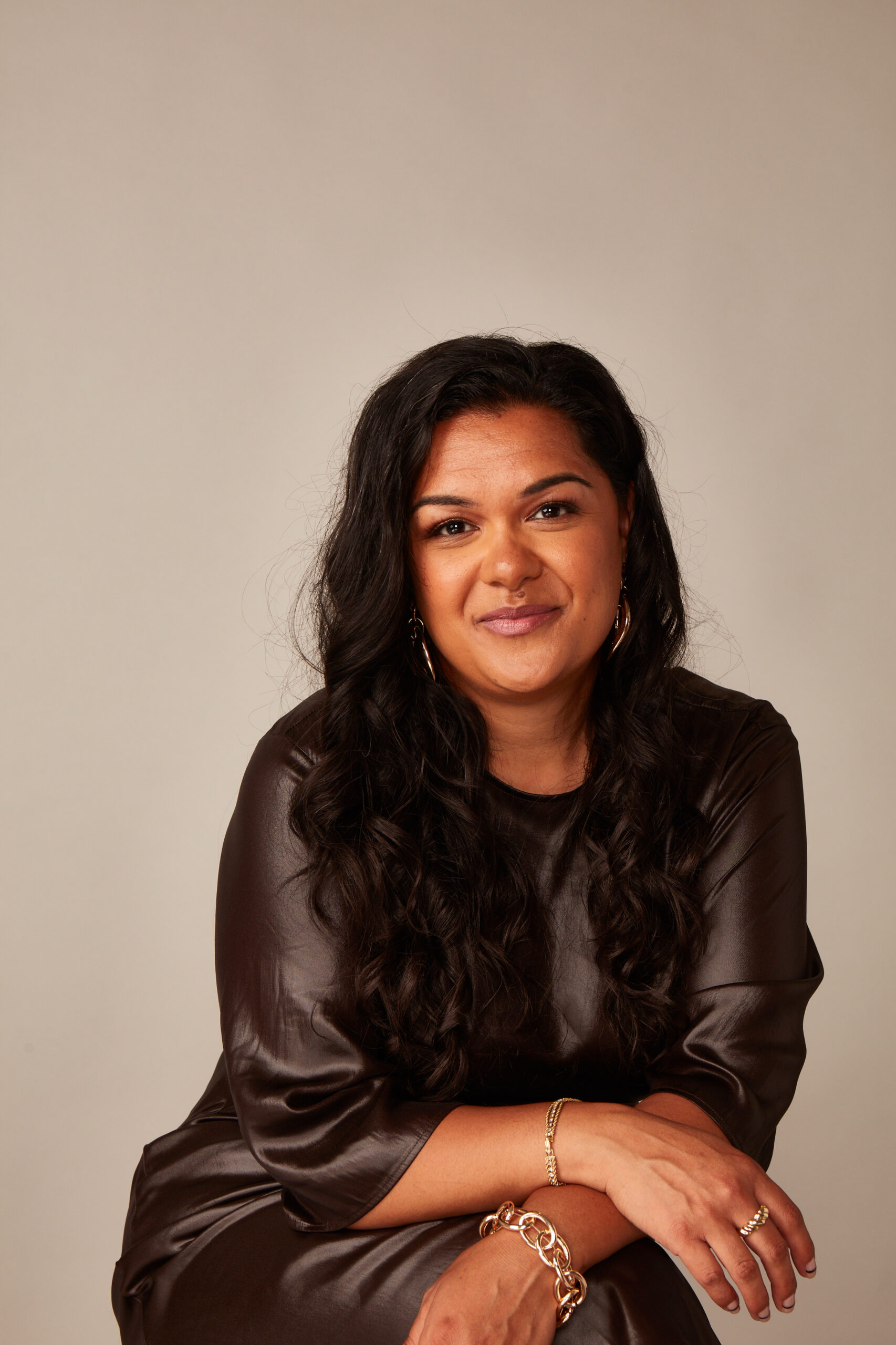 Stacy Lee Kong, author for Three Magazine, posing in a stylish brown outfit with gold jewelry, showcasing contemporary fashion and lifestyle themes.