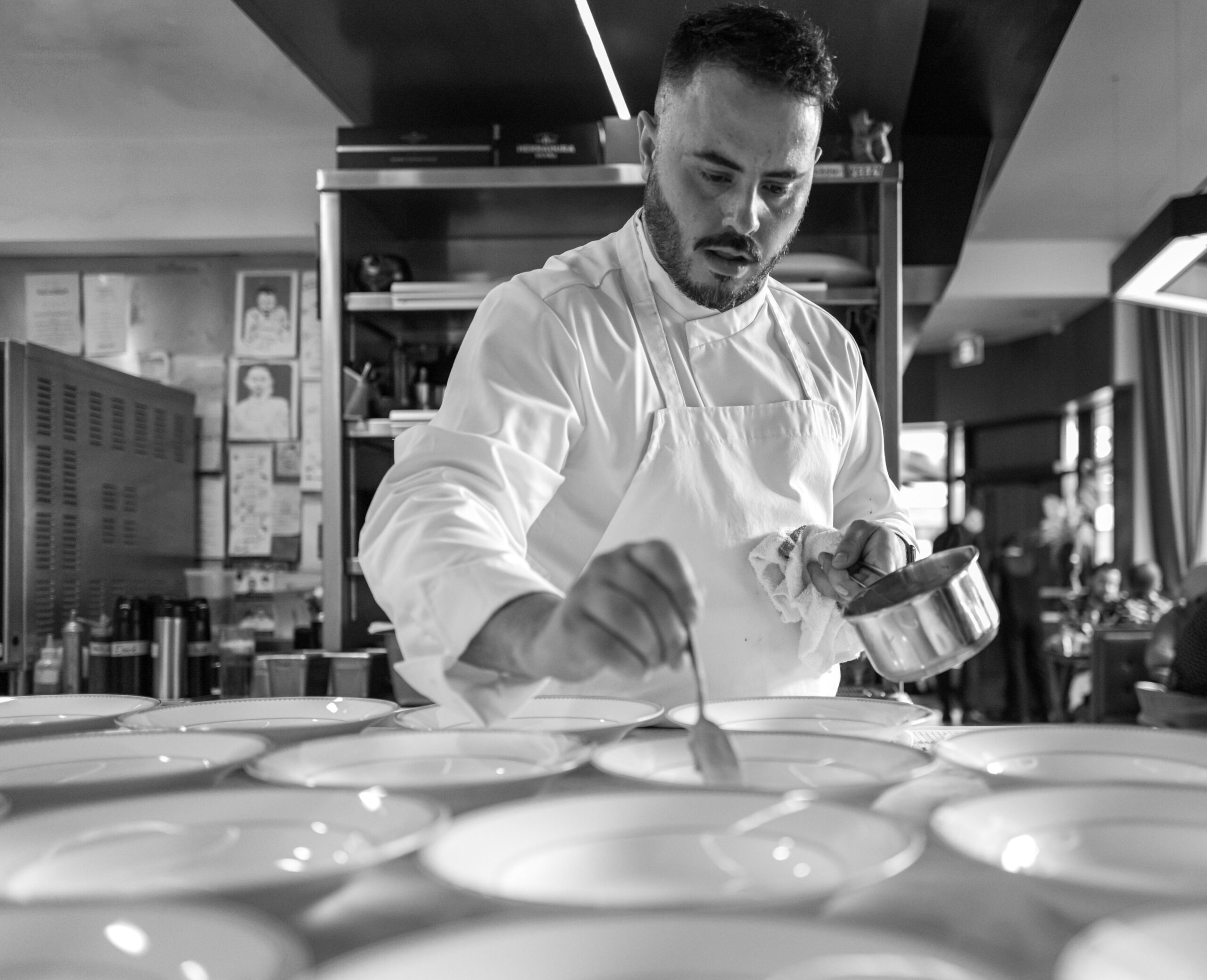 Chef preparing dishes in a restaurant kitchen, focusing on plating with a spoon and sauce, reflecting the artistry of third-culture cuisine.