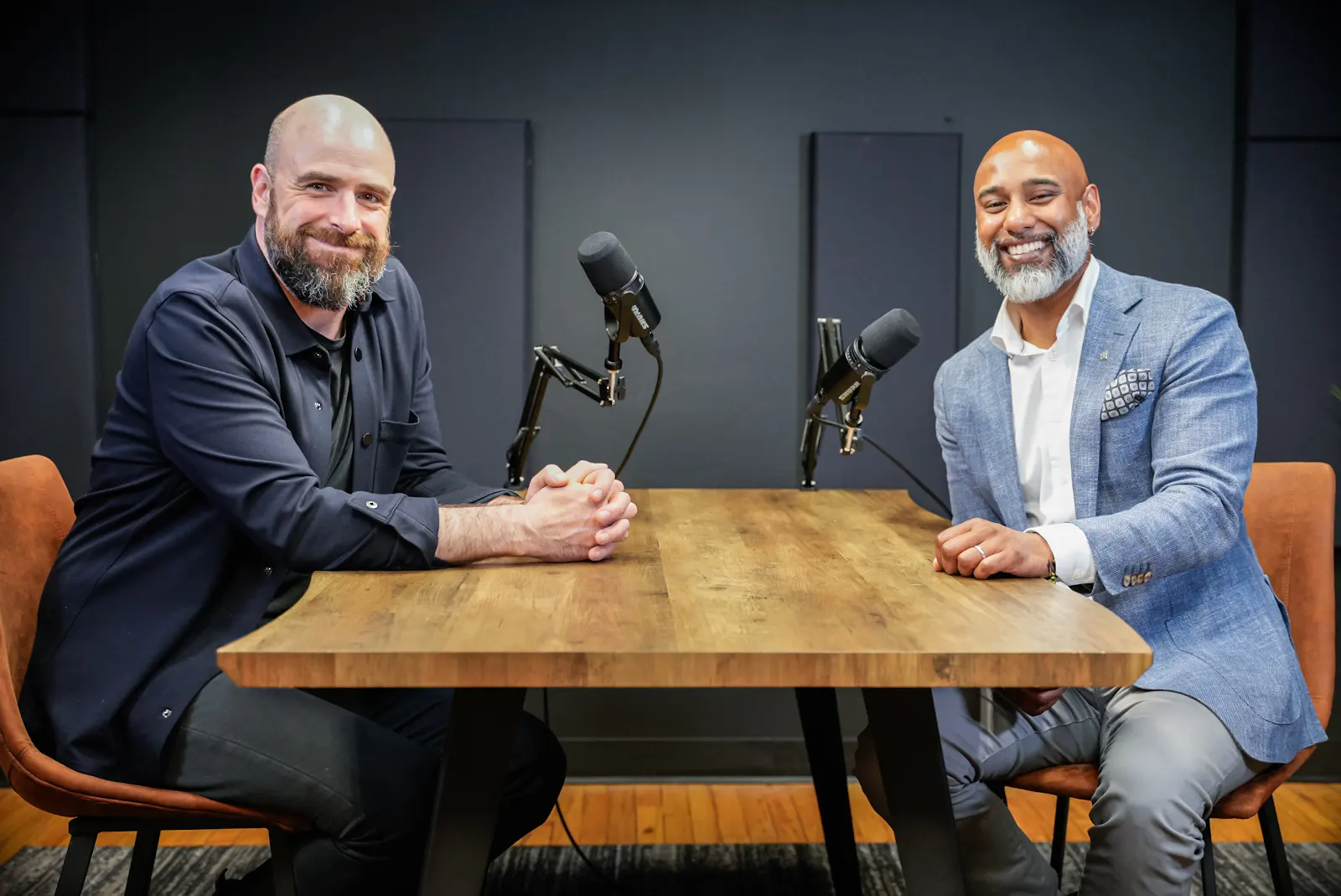 Two men seated at a wooden table in a podcast studio, engaging in conversation, with microphones positioned for recording, reflecting themes of entrepreneurship and venture capital discussions.