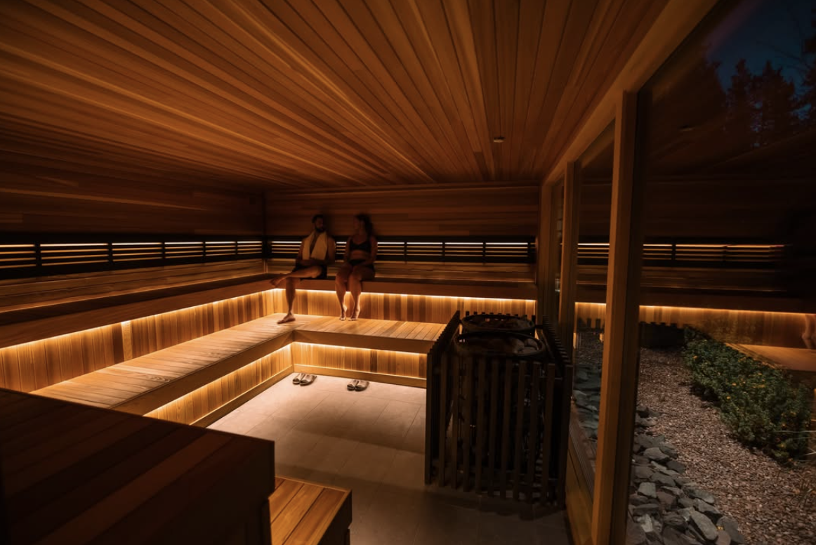 Couple relaxing in a modern sauna with warm wood paneling and ambient lighting, emphasizing wellness and luxury spa experiences.