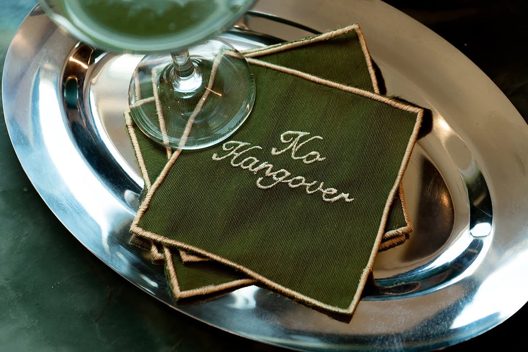 Green napkins with "No Hangover" embroidered, placed on a silver tray beside a cocktail glass.