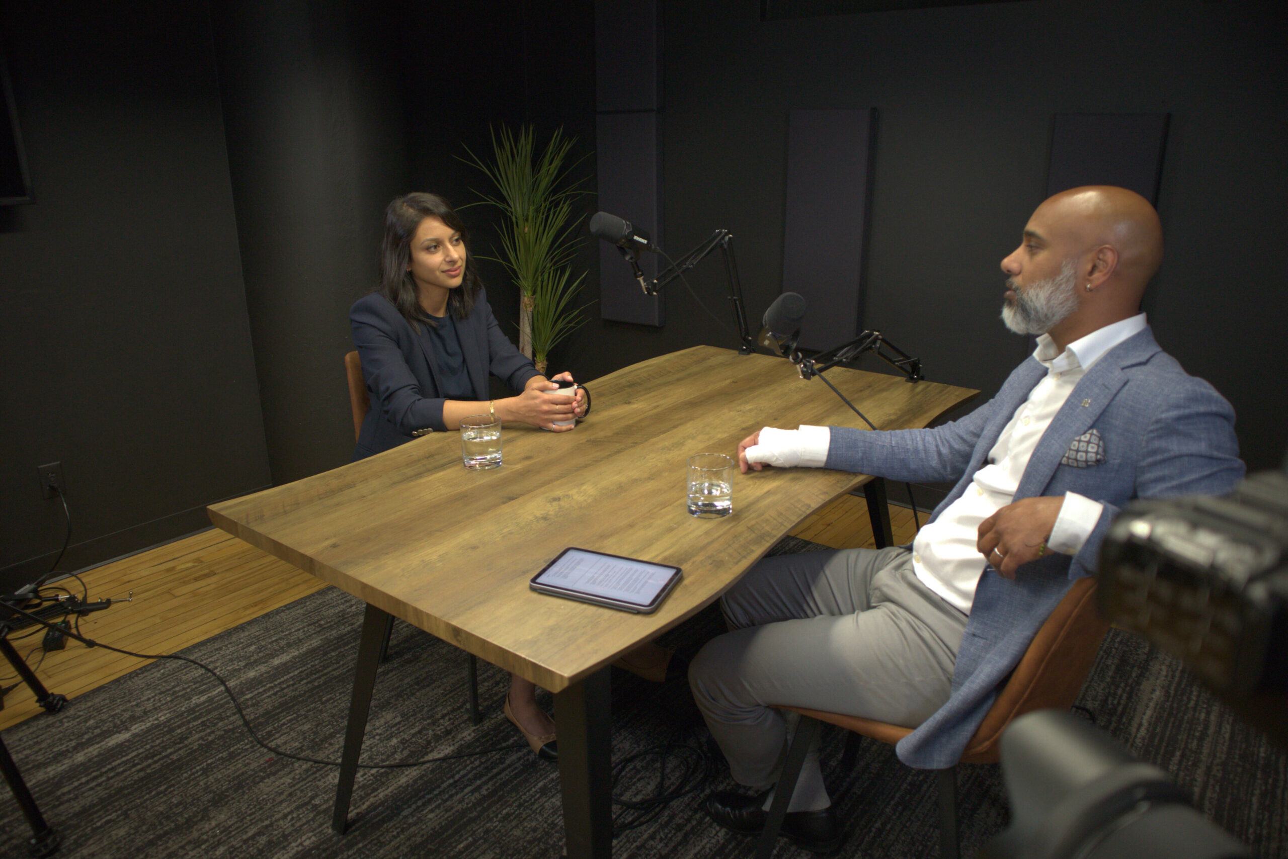 Podcast interview setting featuring Dunya Al Hashar discussing parenting and resilience in the UAE with a host, surrounded by microphones and a modern decor.