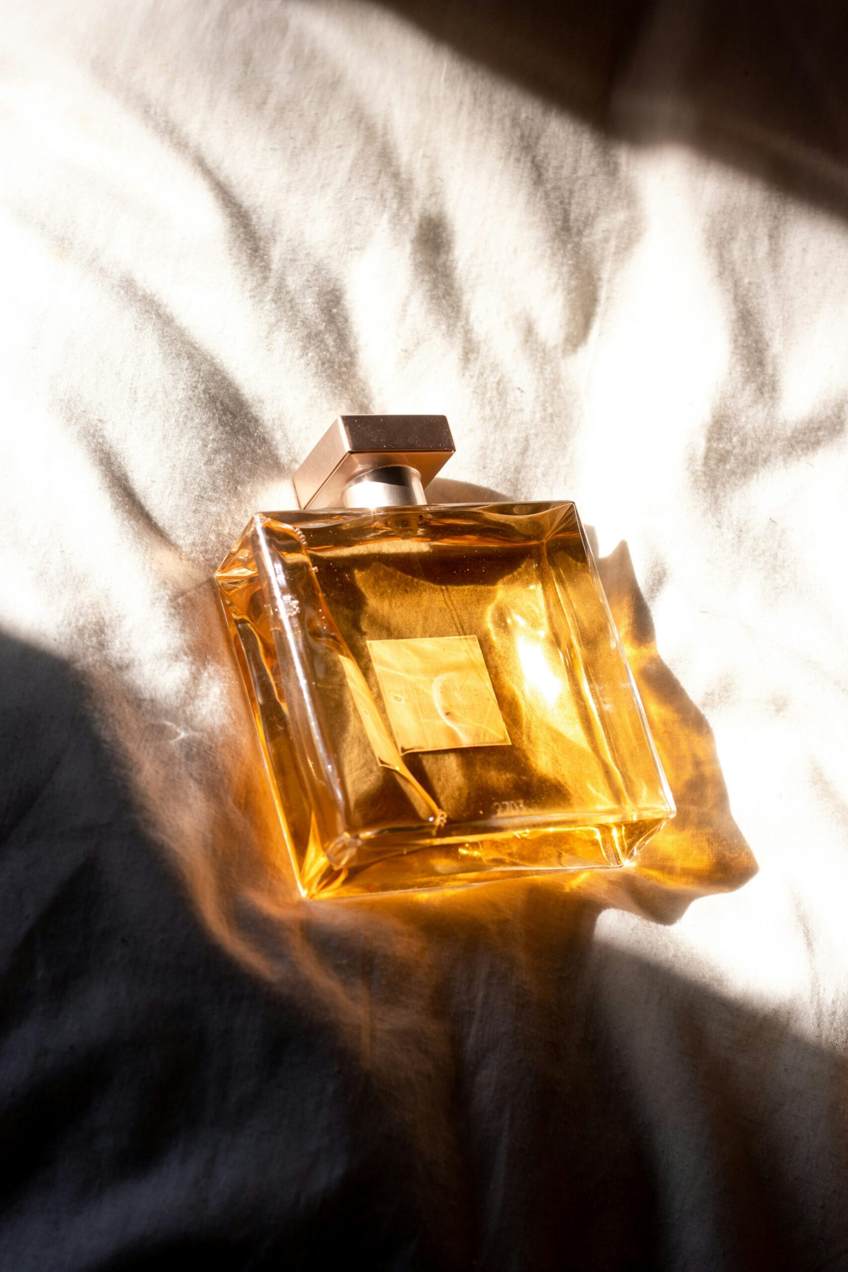 Perfume bottle with golden liquid resting on soft fabric, reflecting the allure of summer scents and contemporary fragrance trends.