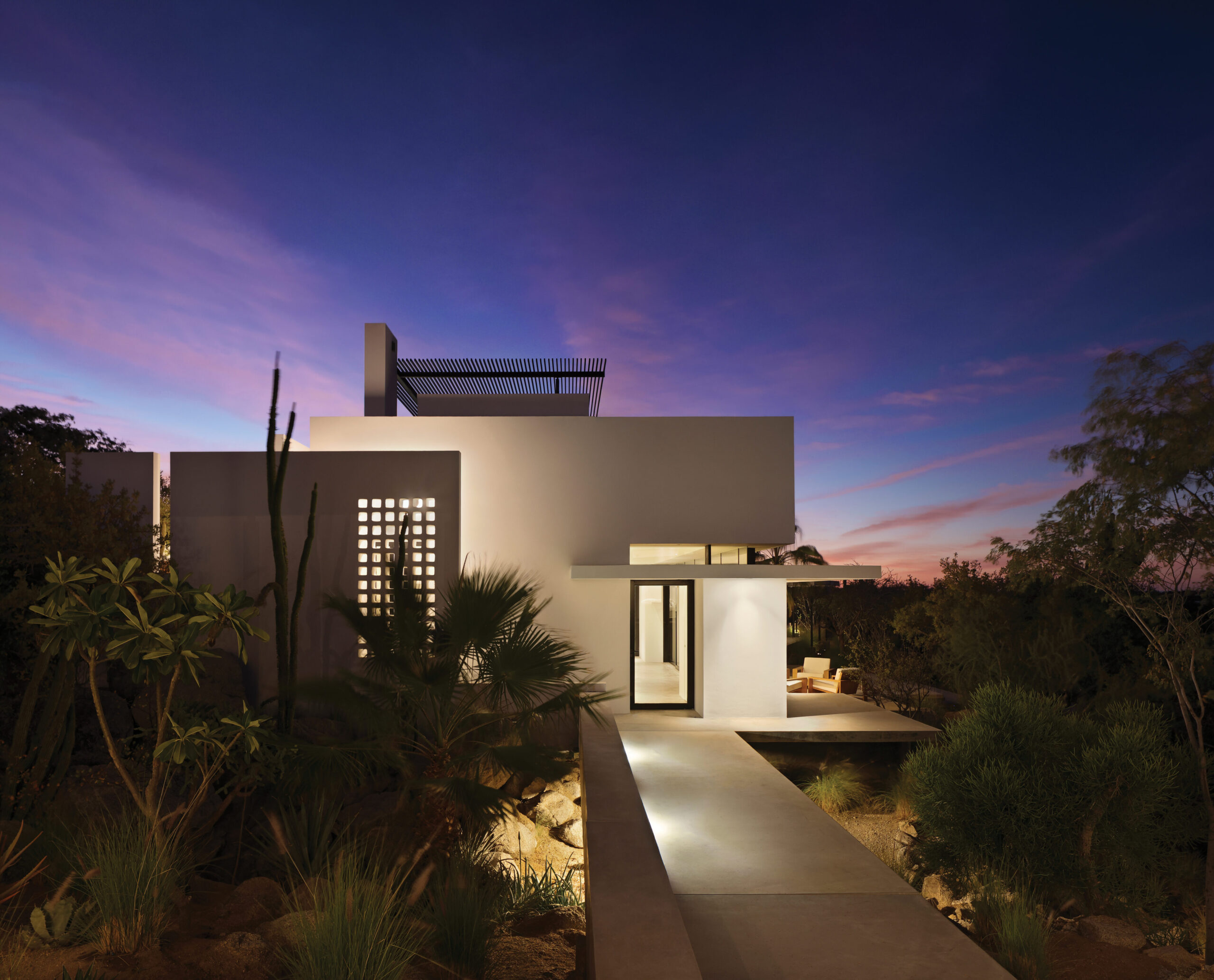 Modern architectural design of a nature-forward home in Mexico, featuring a sleek exterior, desert landscaping, and an evening sky with vibrant colors, reflecting themes of harmony with nature and intentional living.