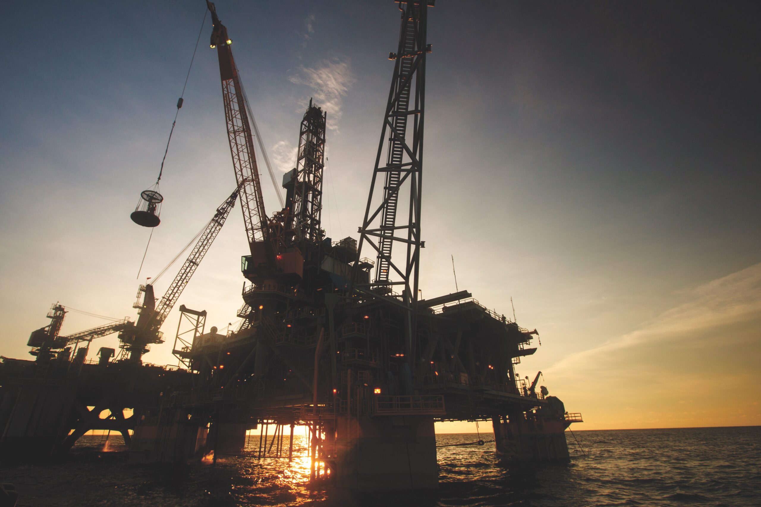 Offshore oil drilling rig silhouetted against sunset, illustrating the energy sector's impact on global markets, relevant to ExxonMobil's discovery in Guyana.