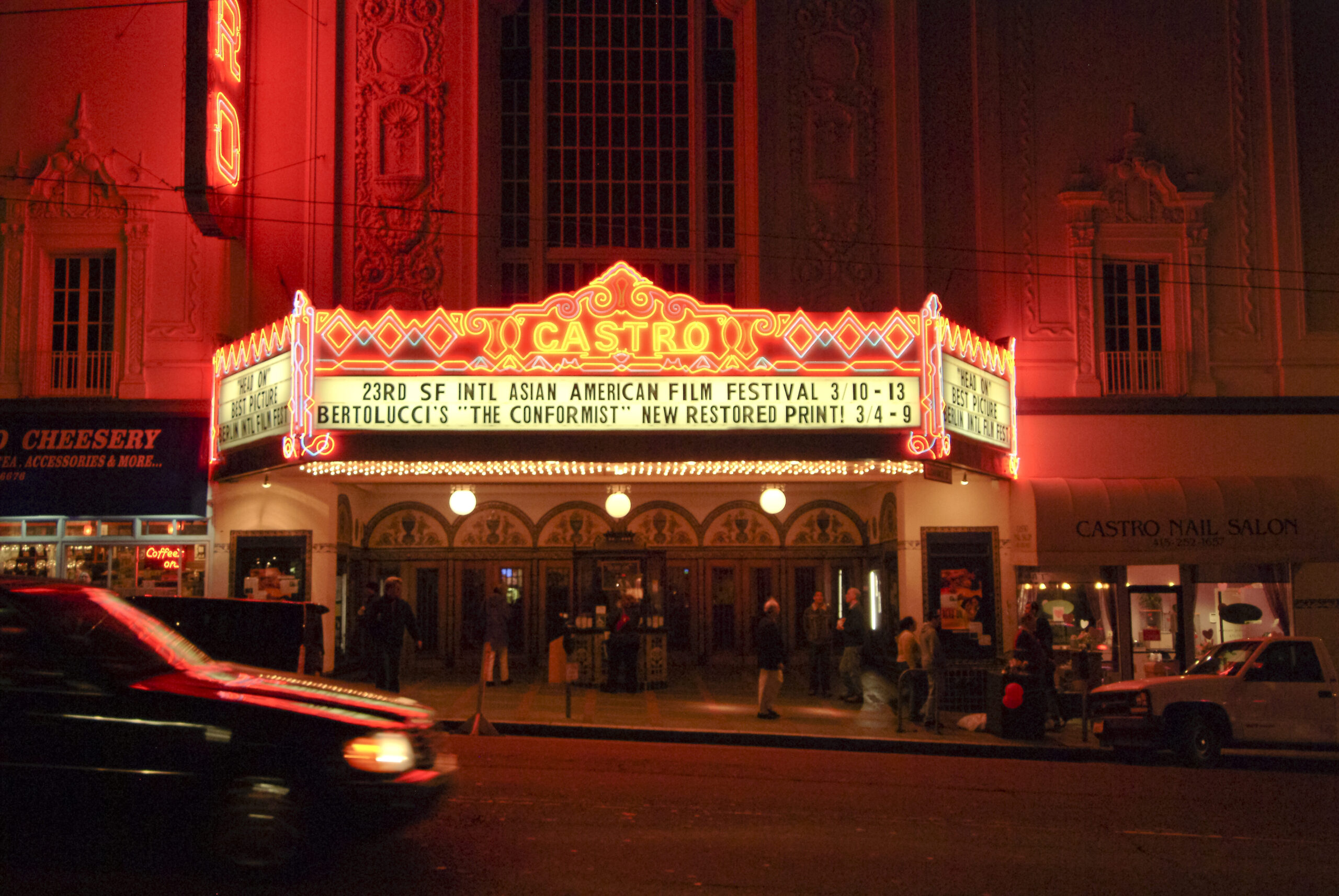 Castro Theatre marquee featuring the 23rd SF International Asian American Film Festival and Bertolucci's "The Conformist," illuminated at night with pedestrians nearby.