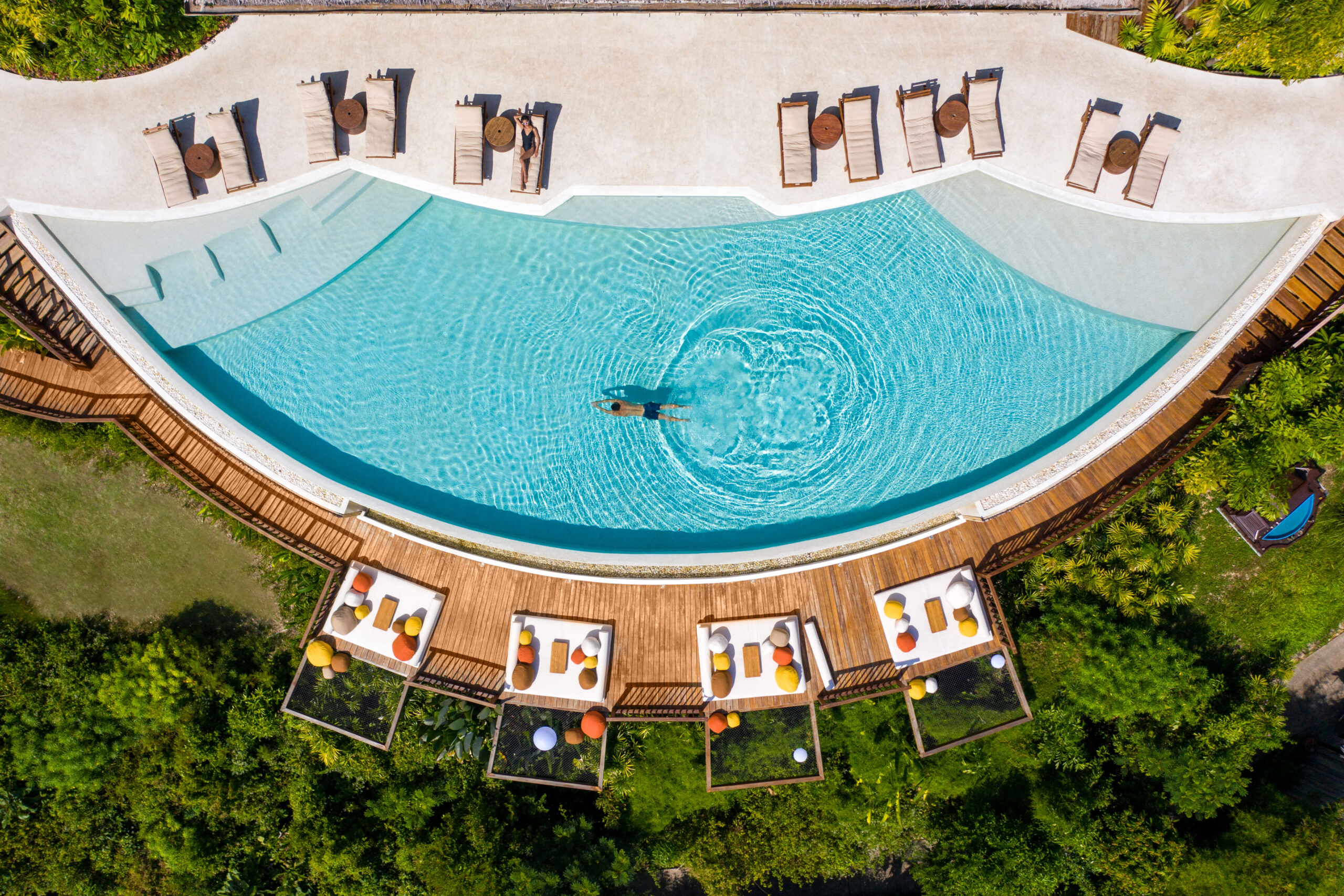 Aerial view of a luxurious pool surrounded by modern lounge chairs and vibrant cushions, set in a lush tropical landscape, illustrating Thailand's high-end hospitality and travel allure.