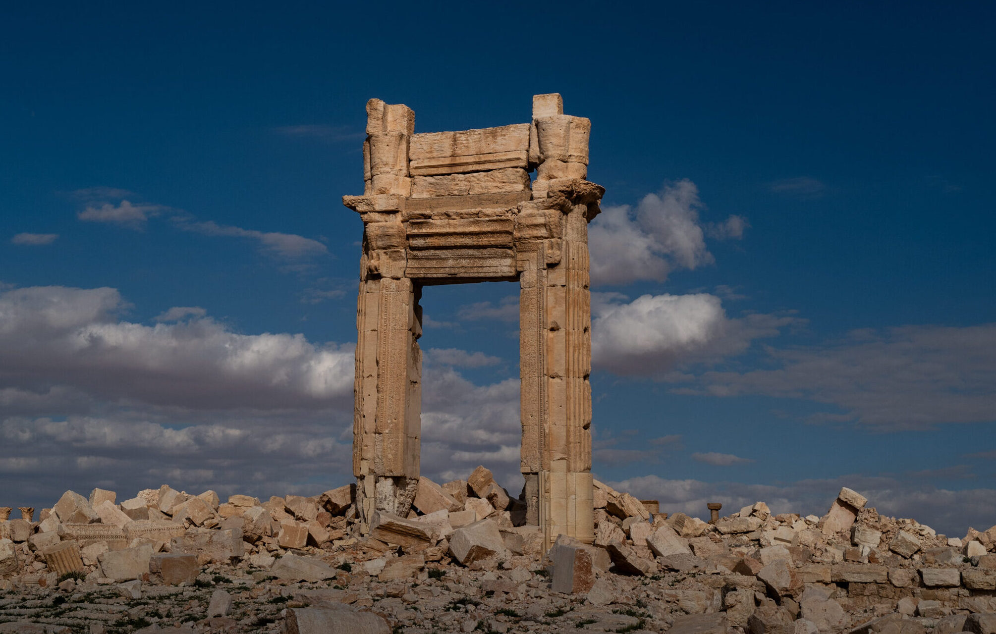 Ancient archway ruins against a dramatic sky, symbolizing cultural preservation in war-torn regions.