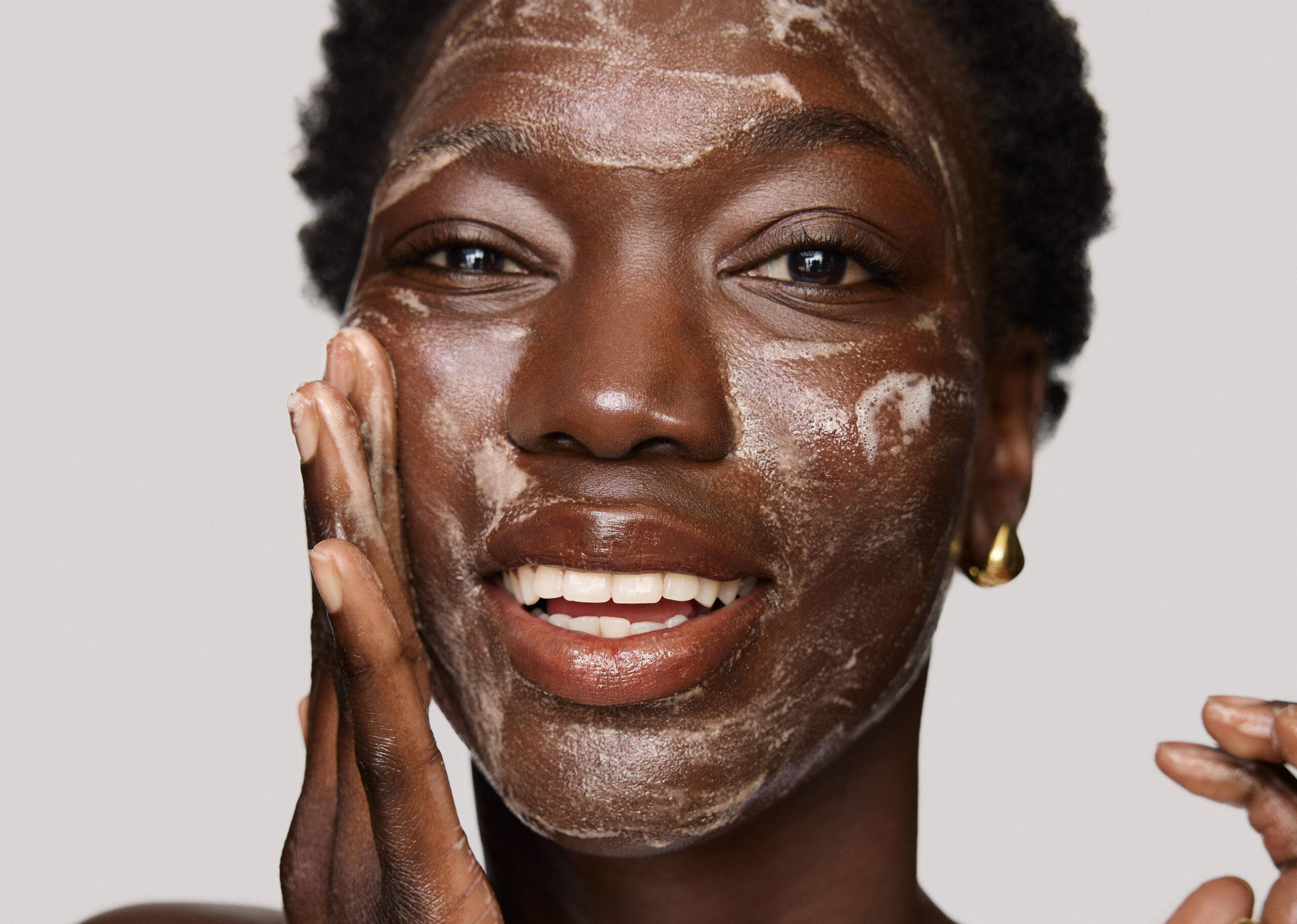 Woman applying a facial cleanser with a radiant smile, showcasing skincare routine and beauty trends.
