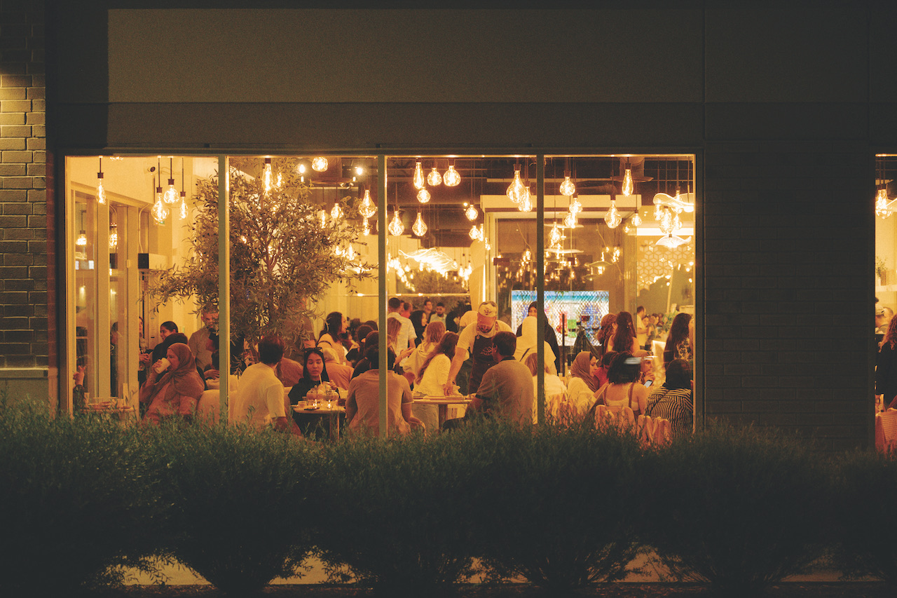 Crowded coffee house interior with patrons enjoying drinks, warm lighting, and a lively atmosphere, reflecting community and culture.