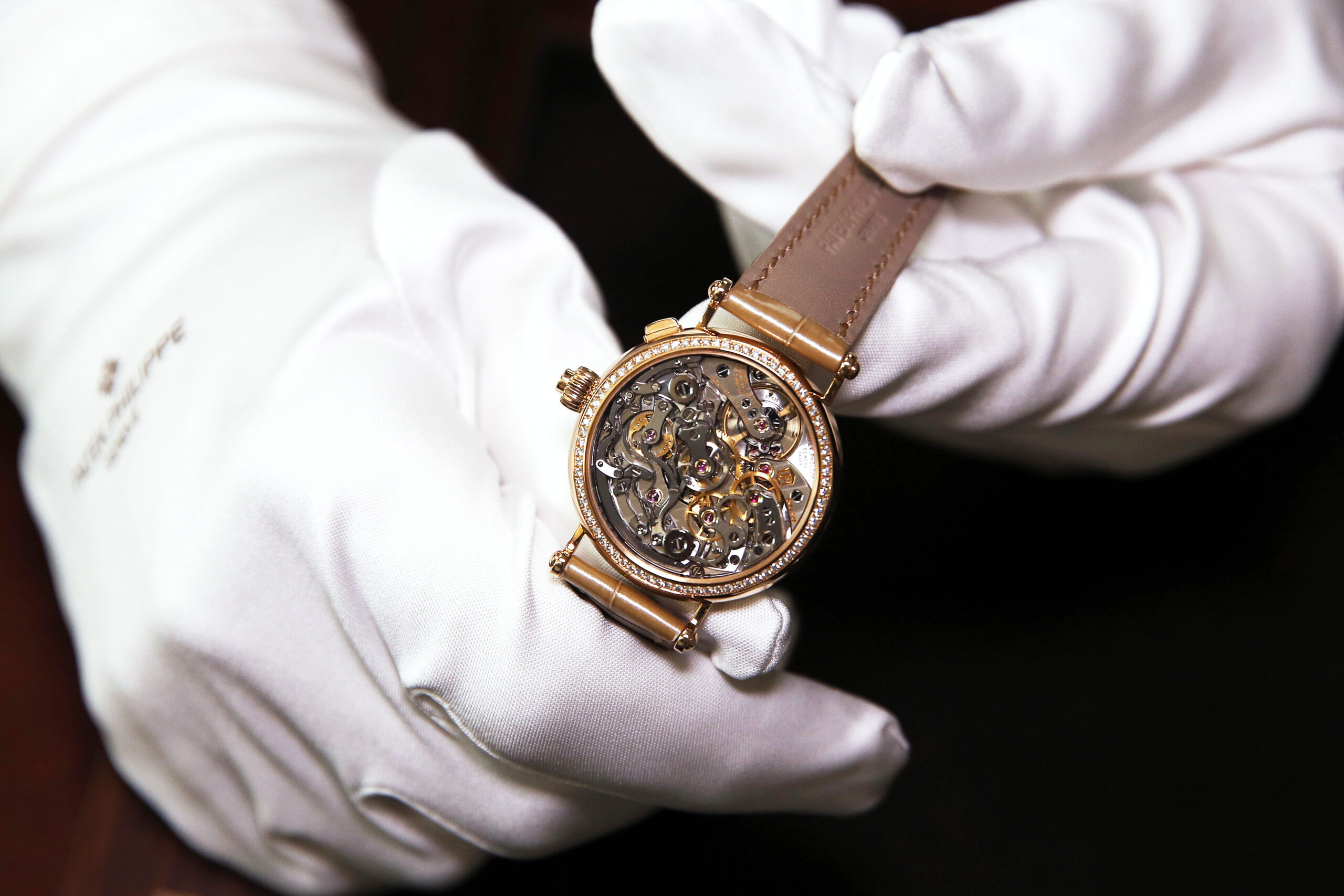 Luxury gold watch with intricate mechanical movement, held in gloved hands, showcasing craftsmanship and design excellence in the luxury watch market.
