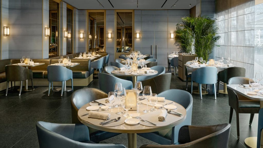 Elegant modern restaurant interior with round tables, upholstered chairs and neatly set dinnerware.