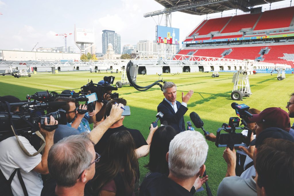 Nick Eaves speaks to press at an empty outdoor soccer stadium. 