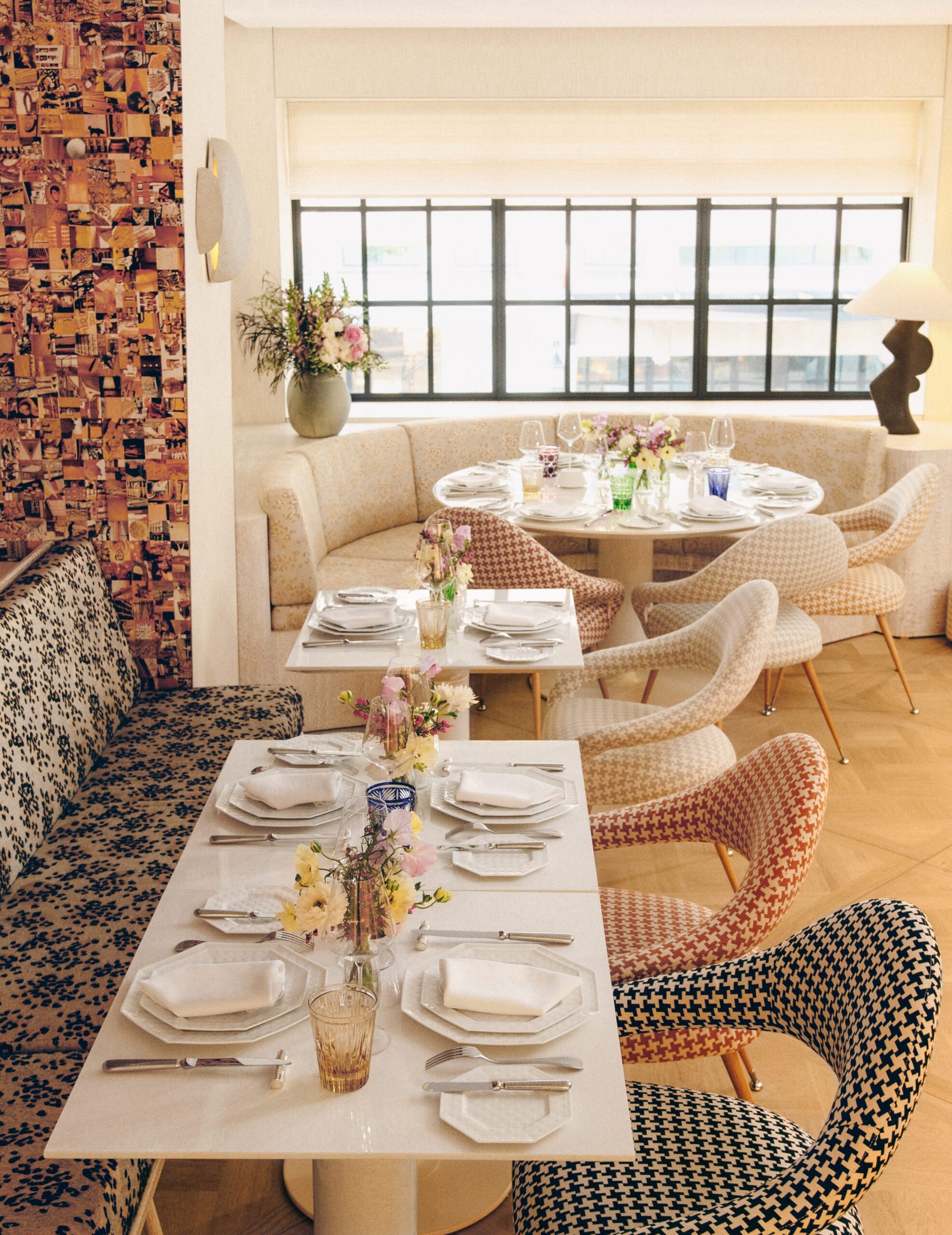 Caf&eacute; interior with patterned chairs, marble dining tables, fresh flowers as centerpieces, and soft natural light from large grid-style windows.