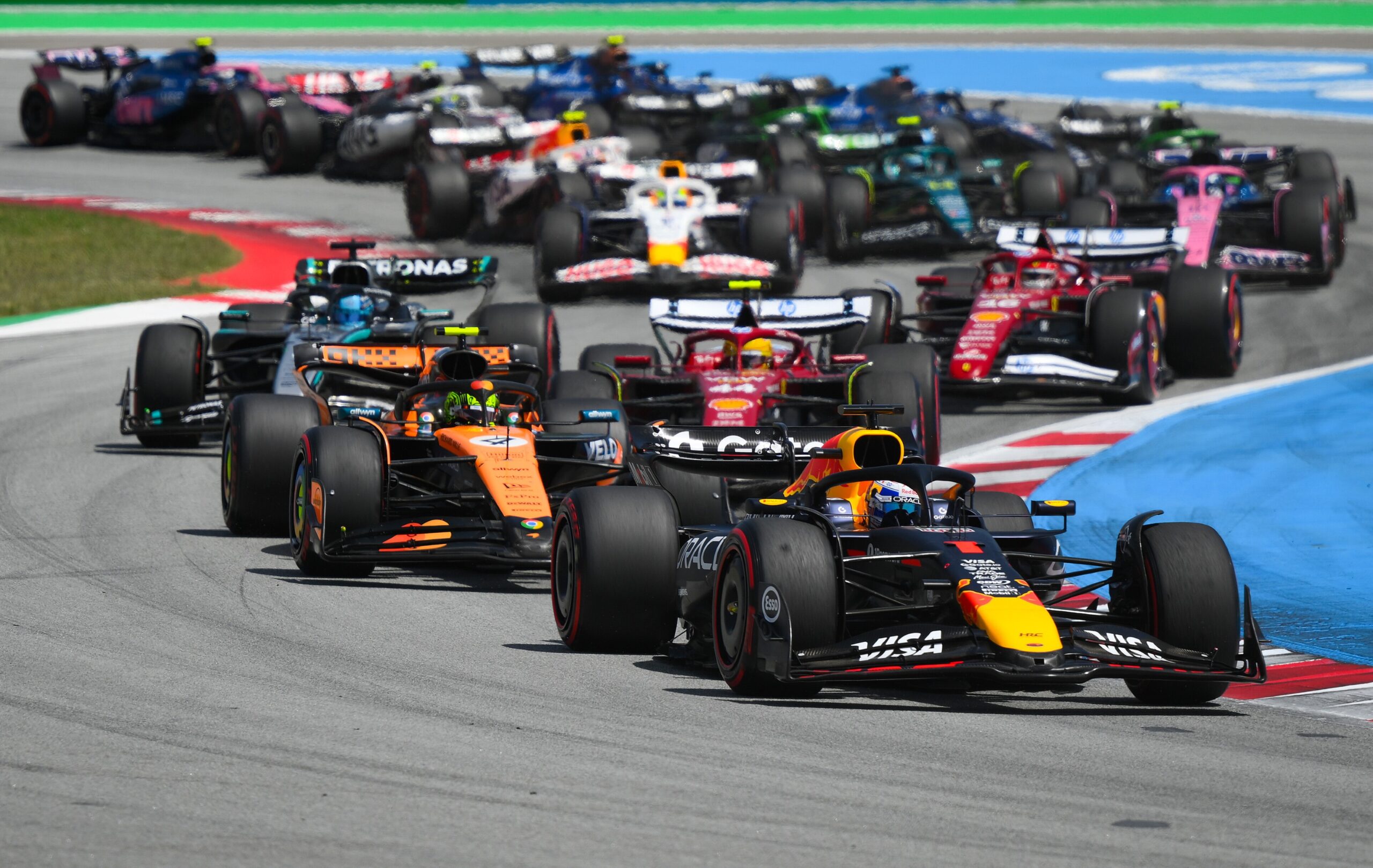 Formula 1 cars racing at the Circuit de Barcelona-Catalunya, showcasing competitive motorsport action with various teams, including McLaren and Red Bull, during a bright day.