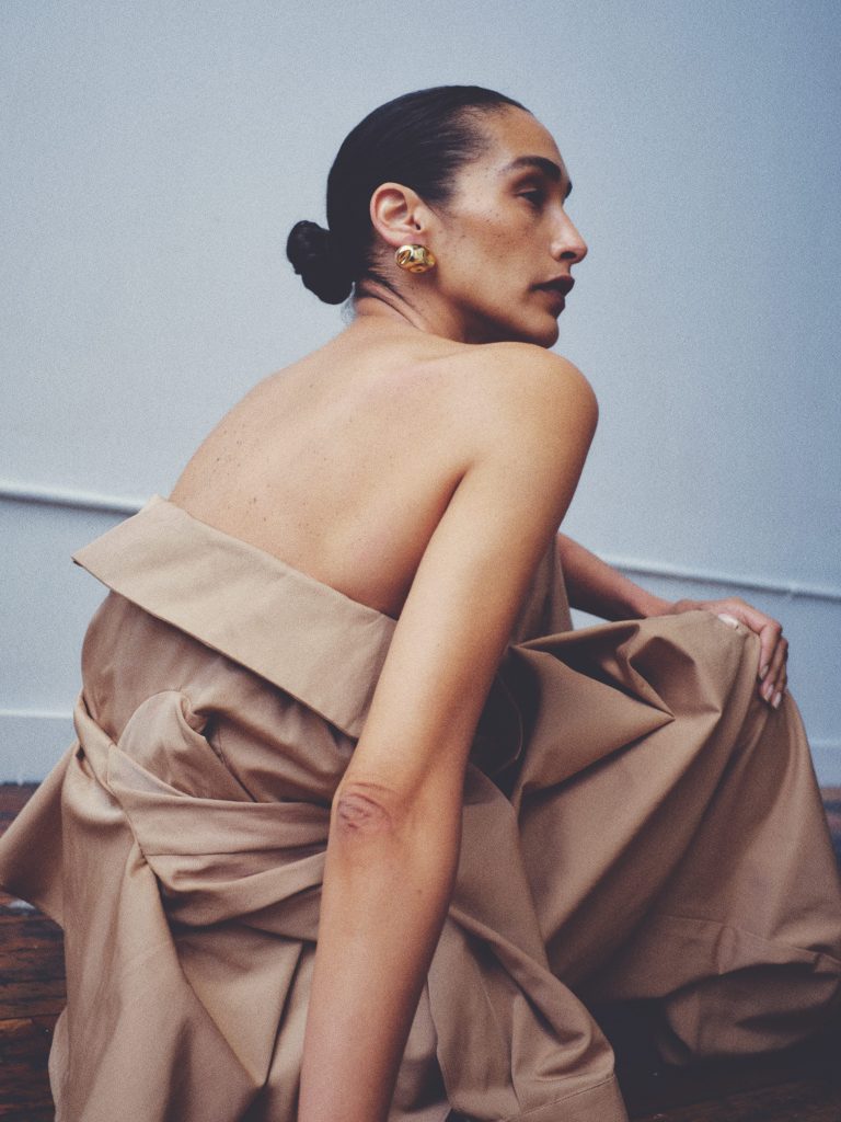 Woman poses wearing a strapless collar top and chunky gold earrings.