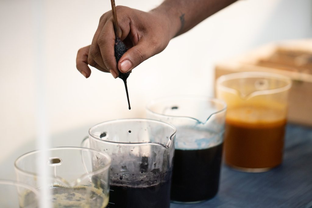 Close up of hand holding a brush and dipping into a clear jar of paint.