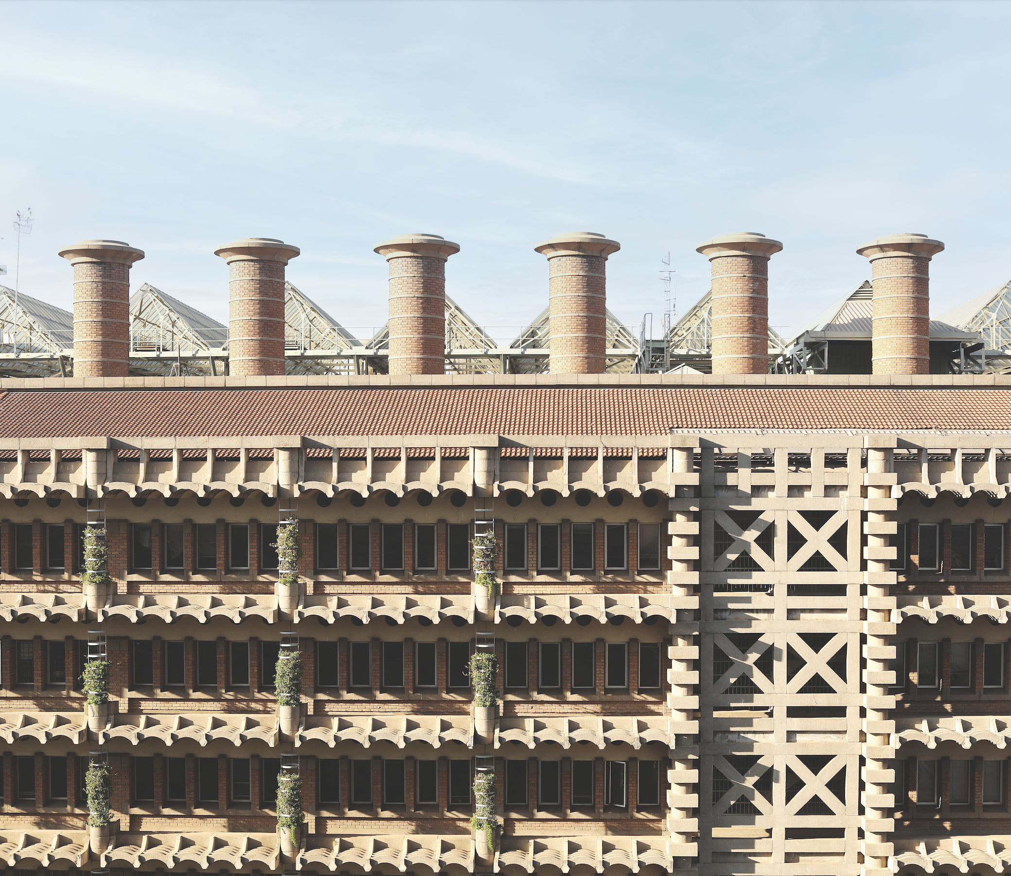 Architectural building with prominent brick fa&ccedil;ade, featuring multiple levels of windows and decorative elements, topped by cylindrical chimneys, reflecting innovative design in addressing climate challenges.