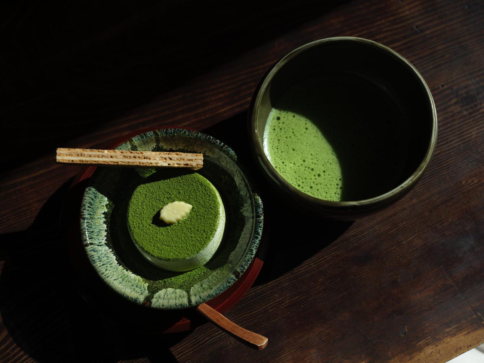 Matcha dessert with a dollop of cream and a wafer stick beside a bowl of matcha tea, set on a wooden table, reflecting culinary innovation in sweets.