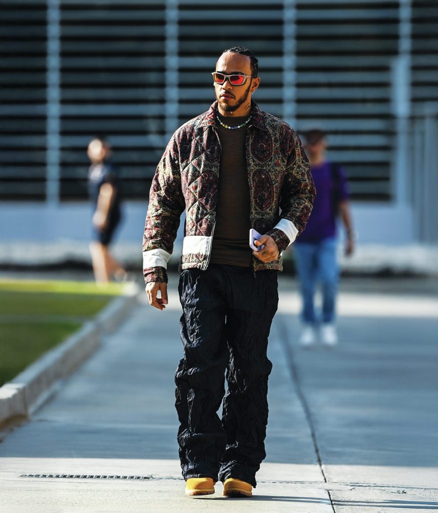 Lewis Hamilton walks outside wearing a printed jacket and black pants.