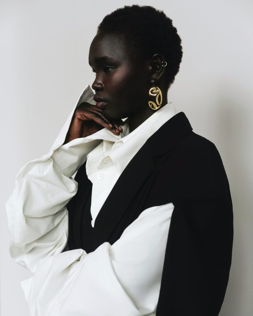 Woman wearing a white button down shirt and a black vest, paired with chunky gold earrings.