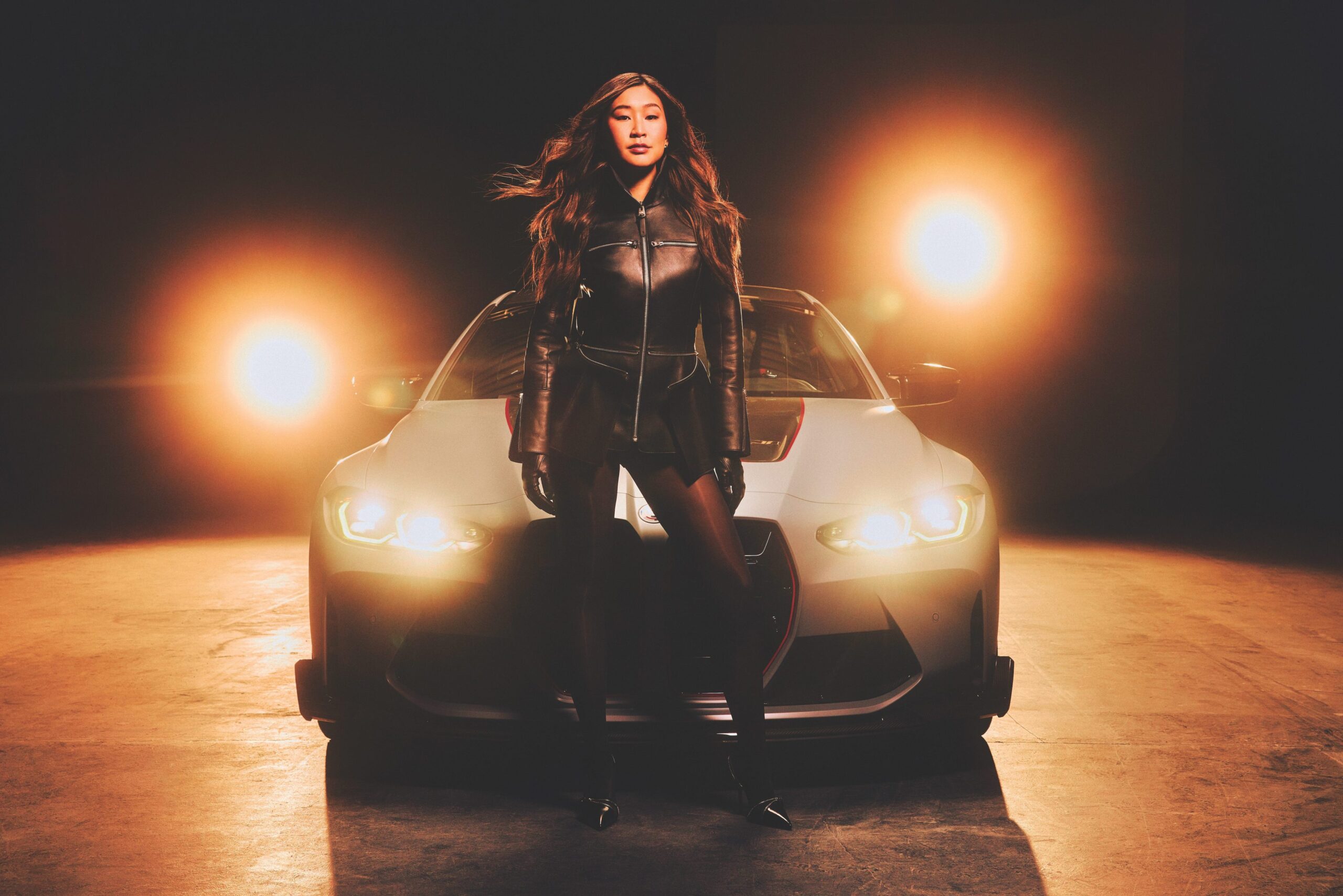Samantha Tan, sports car racer and BMW M Motorsport ambassador, standing confidently in front of a sleek racing car, illuminated by dramatic lighting, showcasing her role in promoting women in motorsports.
