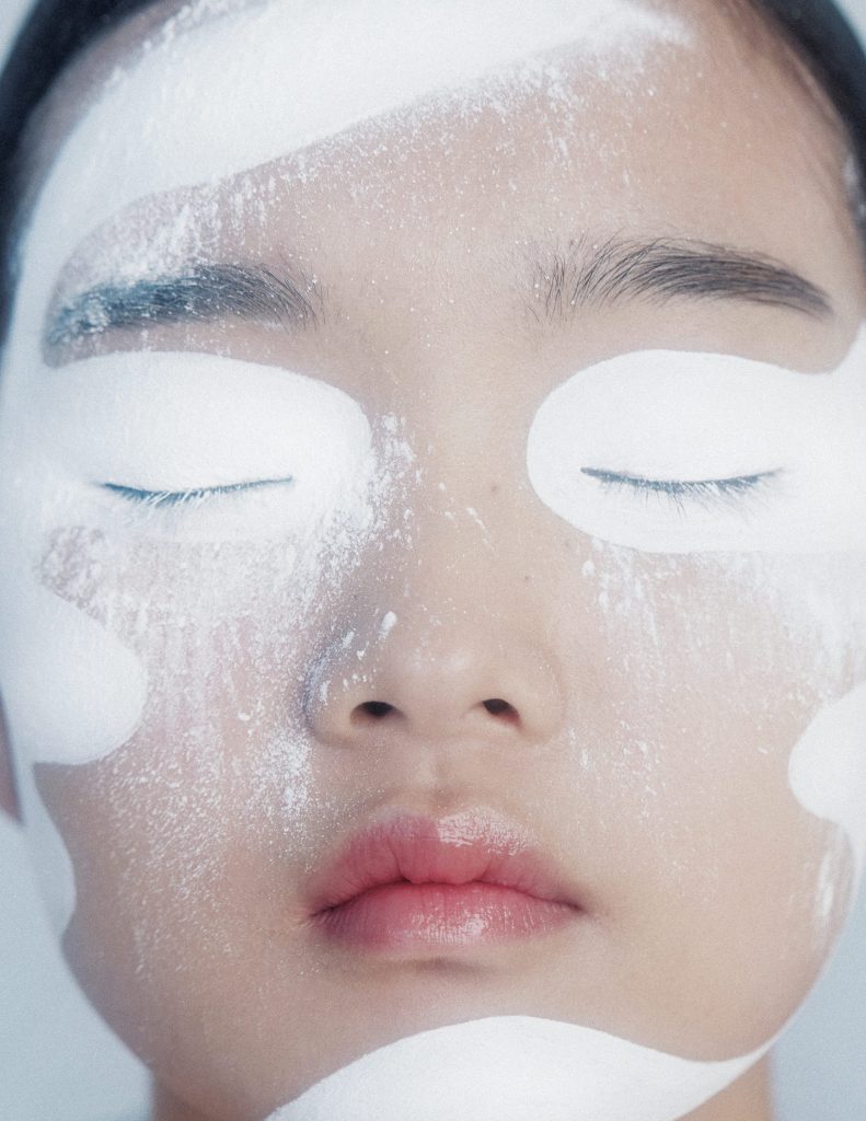 Woman closing her eyes with powdered skincare treatment on her face.
