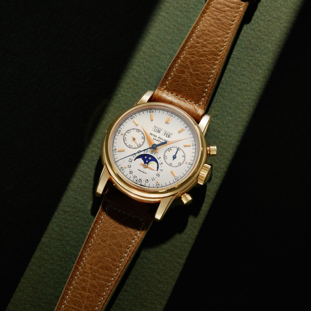 Patek Philippe Grand Complications Annual Calendar watch with gold case and brown leather strap, showcasing a white dial with moon phase indicator and date functions, relevant to the luxury watch market discussion.