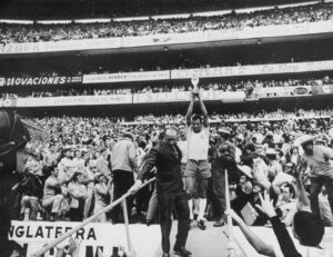 Black-and-white editorial image of a footballer lifting the World Cup trophy in a packed stadium, with the title Against All Odds