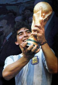 Diego Maradona smiling while lifting the FIFA World Cup Trophy after Argentina’s 1986 World Cup victory.